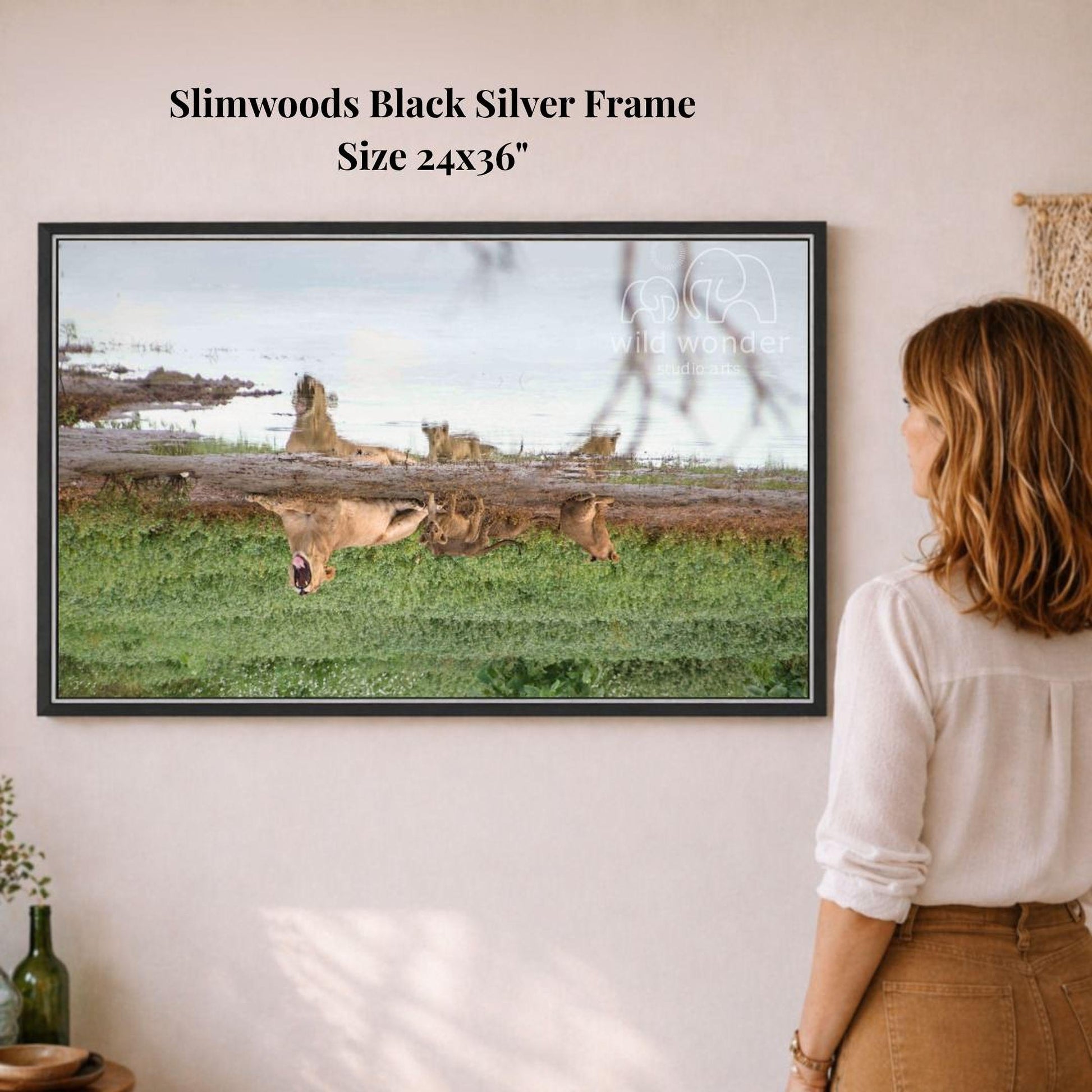 A woman is standing in front of a framed photograph of a group of animals, including giraffes and elephants, in a grassy field.