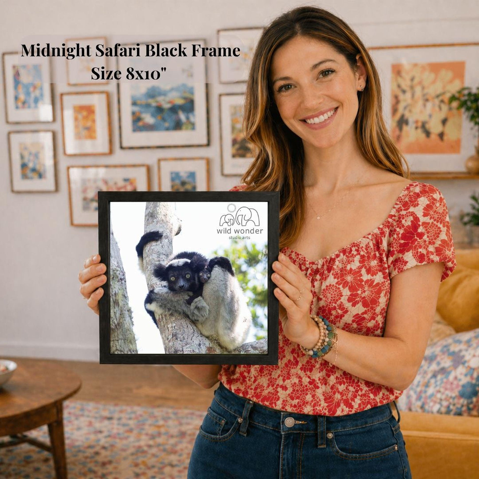 A woman is holding a framed photograph of a monkey in a tree, with a smiling expression on her face.