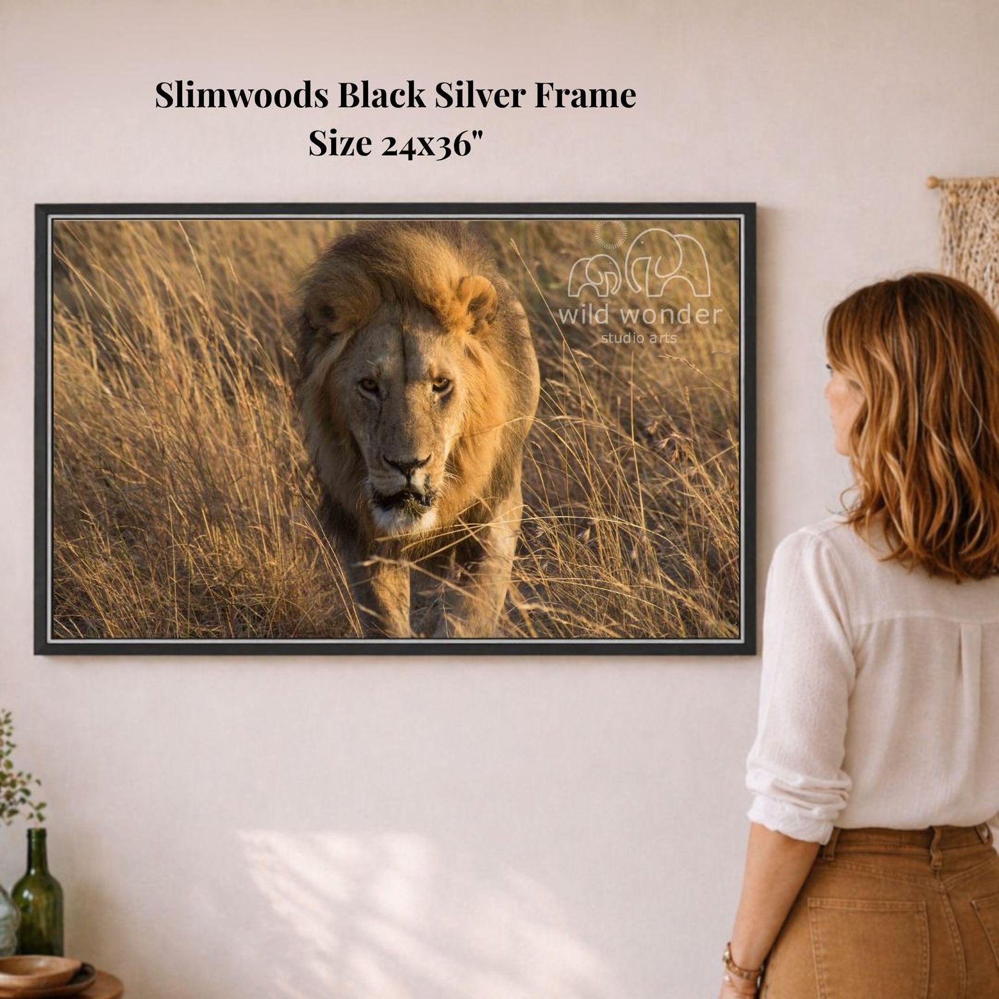 A woman is standing in front of a framed photograph of a lion in a grassy field, looking at the artwork on the wall.