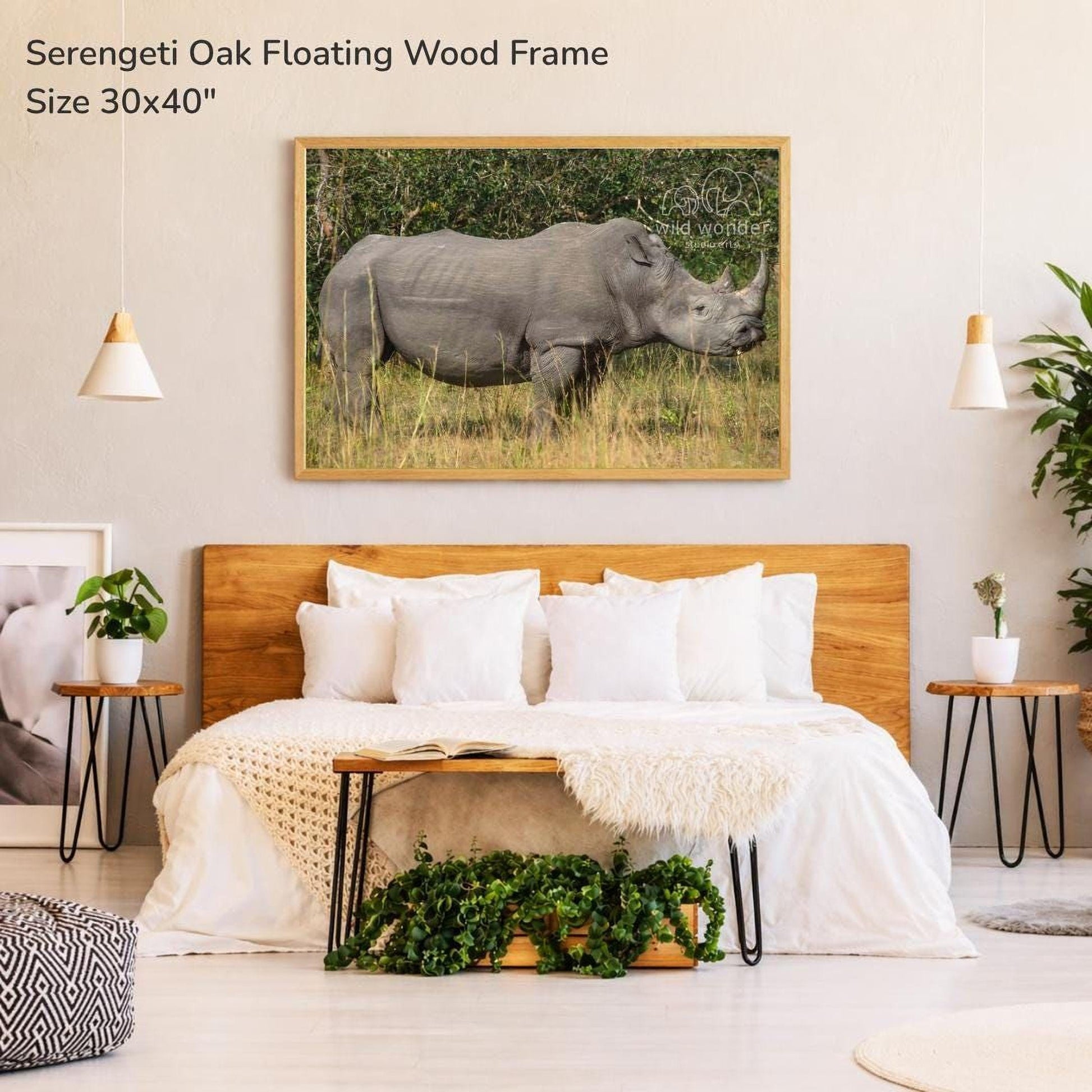 a bedroom with a large wooden headboard and a white bedspread. Above the bed is a framed photograph of a rhinoceros in a grassy field.