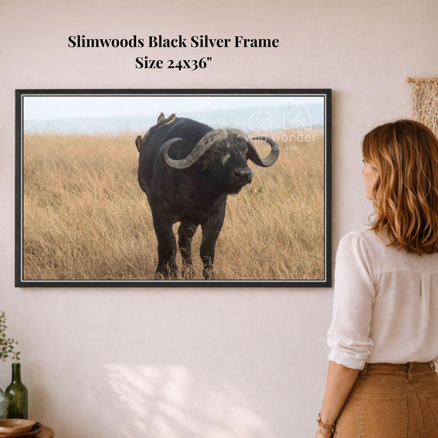 A woman is standing in front of a framed photograph of a black buffalo with large curved horns, which is mounted on a wall.