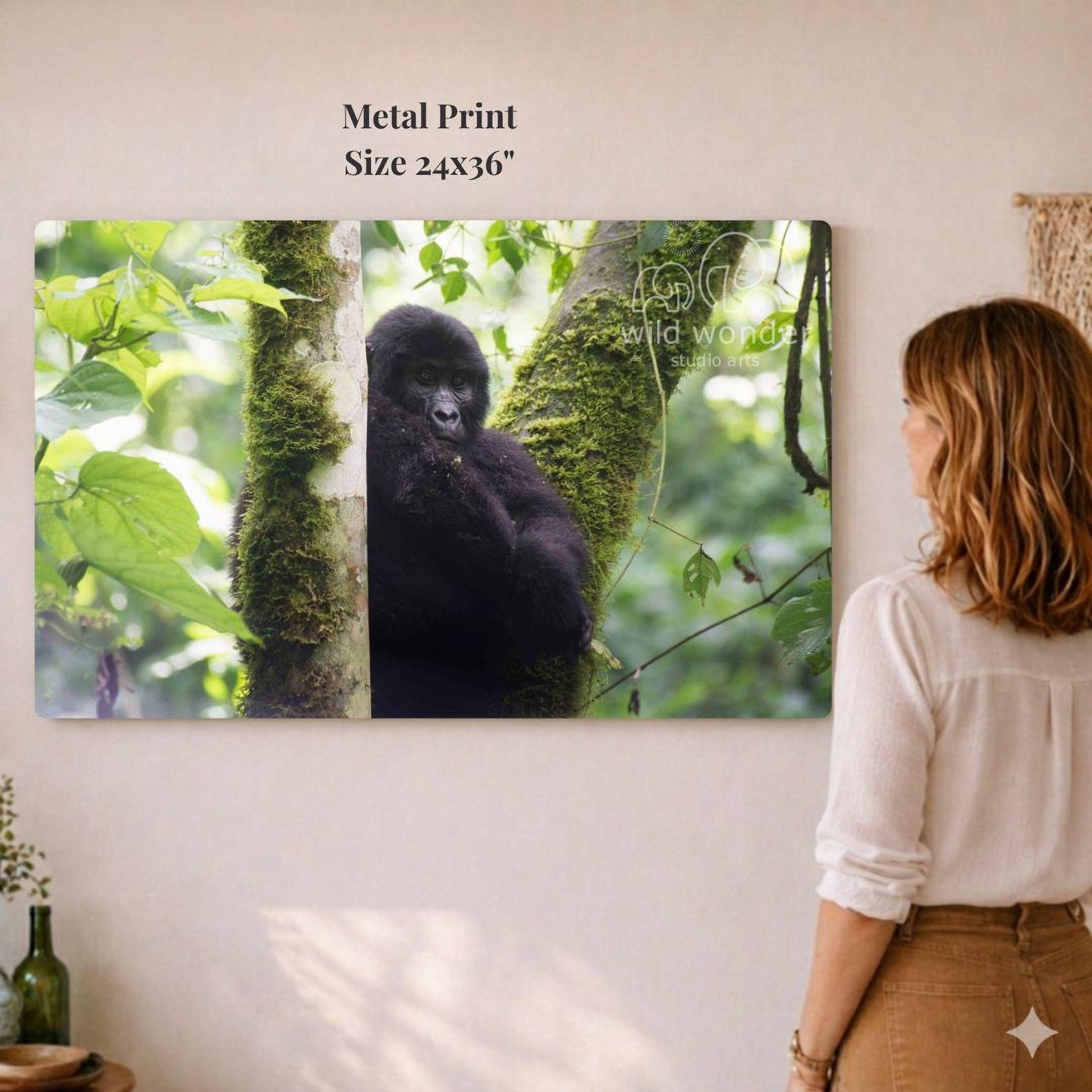 A woman is standing in front of a large metal print depicting a gorilla in a lush, green forest environment.