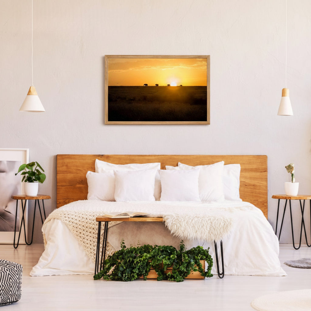 a serene bedroom scene with a large wooden headboard, a white bedspread, and a framed picture of a sunset over a field. The room has a minimalist and modern design, with pendant lights hanging above the bed and a plant on a side table.