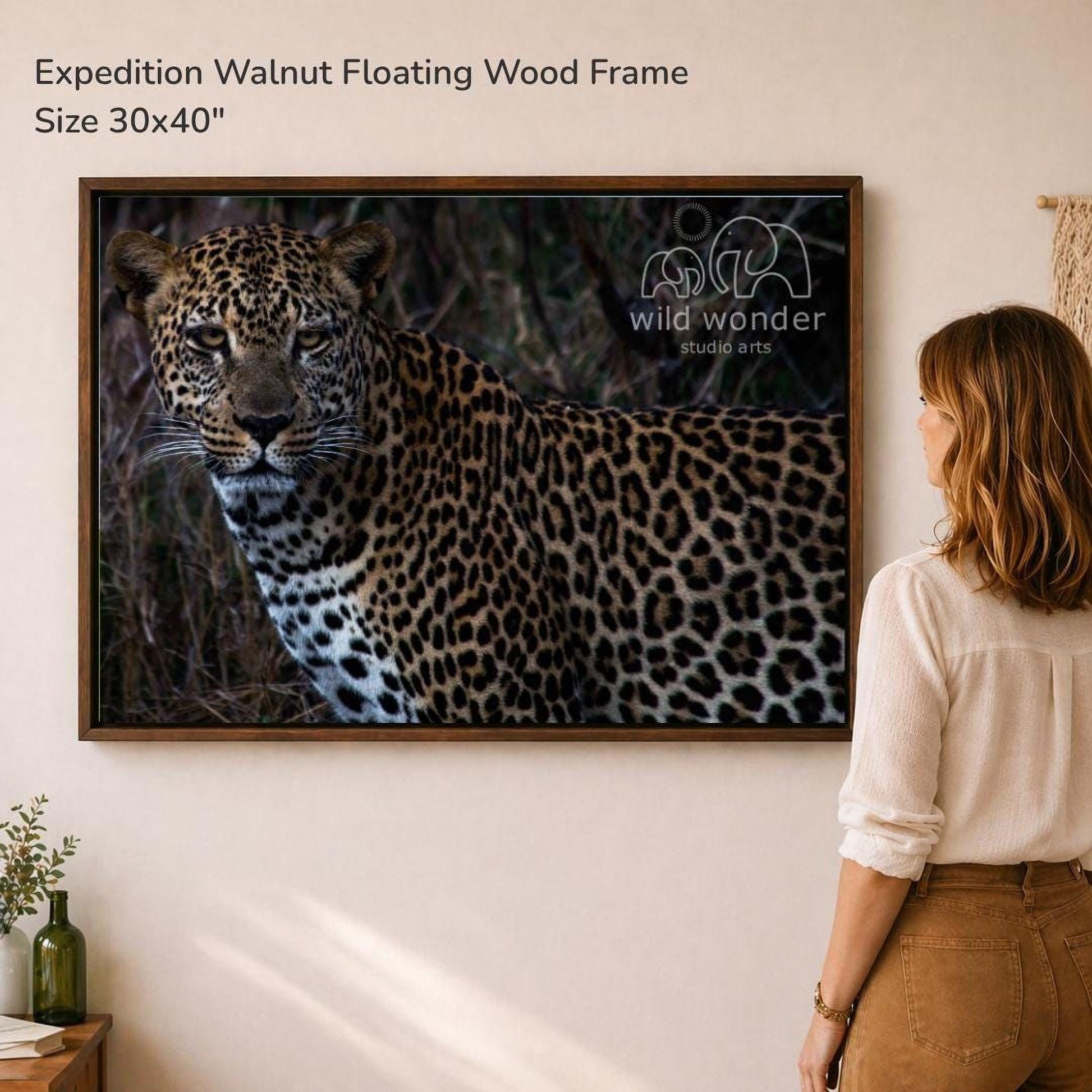 A woman is standing in front of a large framed photograph of a leopard, looking at the artwork on the wall.