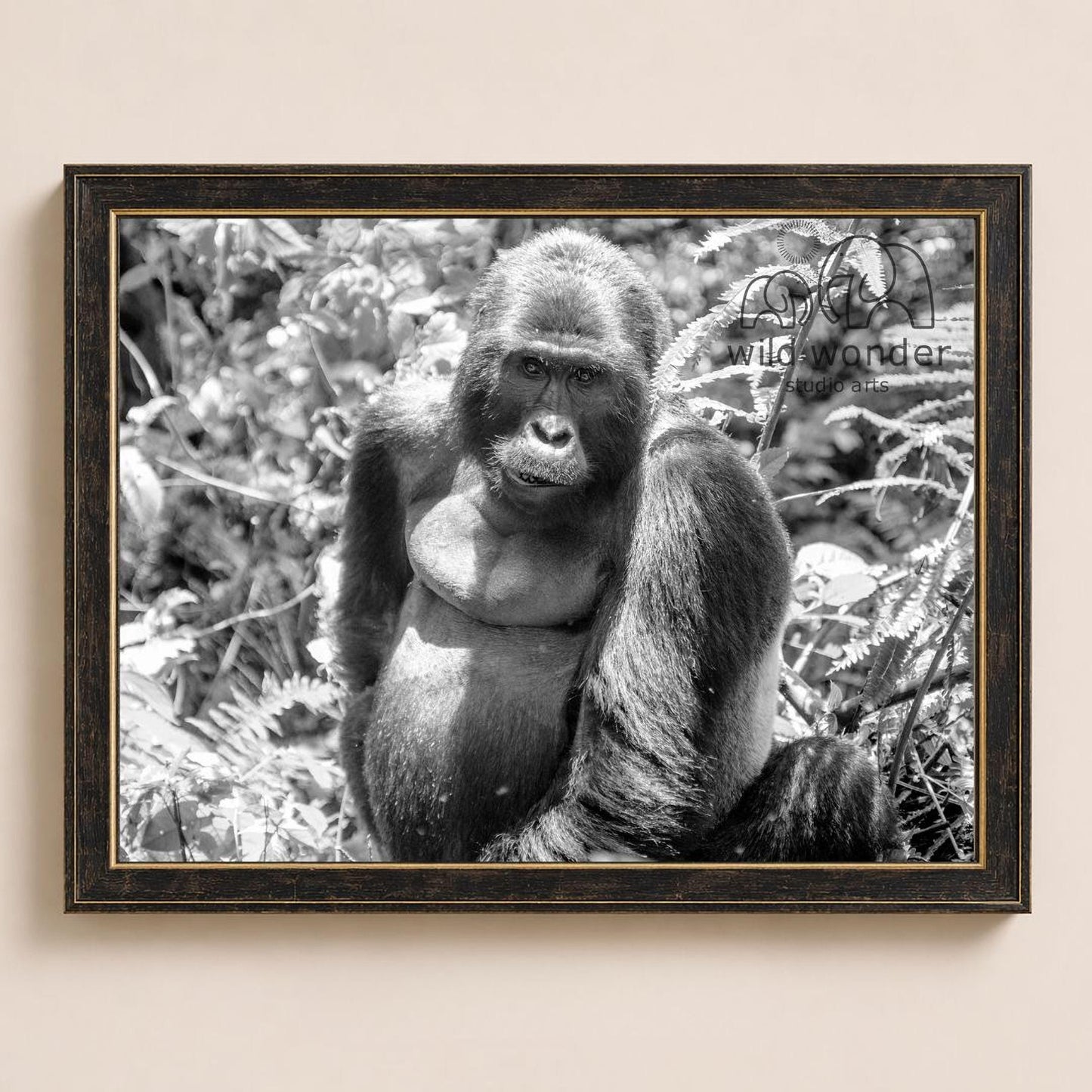 A black and white photograph of a gorilla sitting in a natural setting, surrounded by foliage.