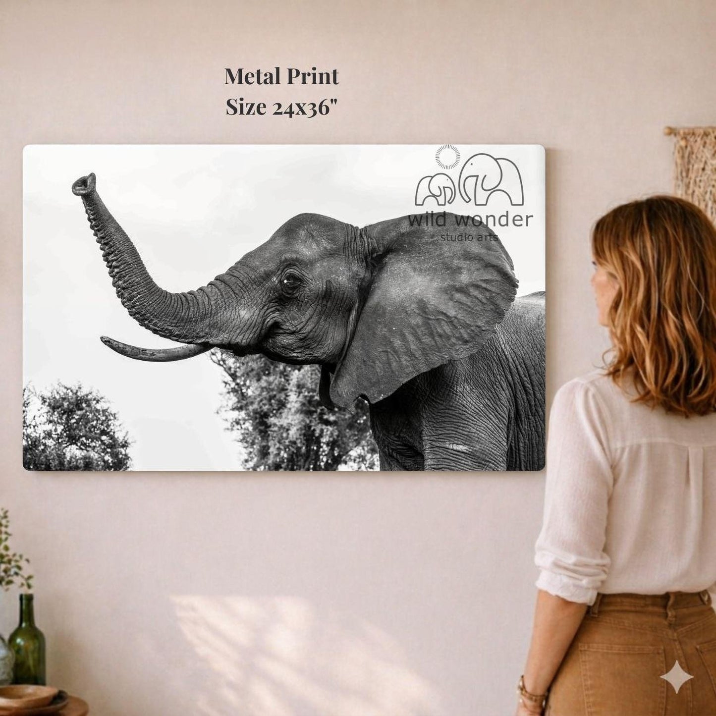 A woman is standing in front of a large metal print of a black and white photograph of an elephant, which is hanging on a wall.