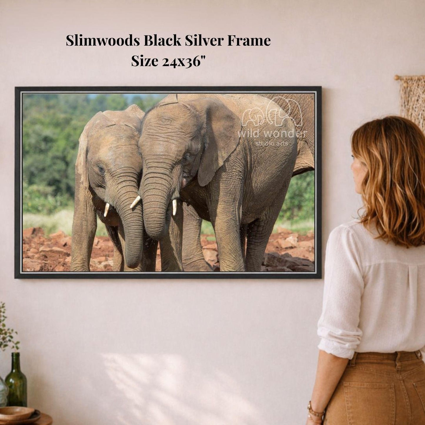 A woman is standing in front of a framed photograph of two elephants, one larger and one smaller, in a natural setting.