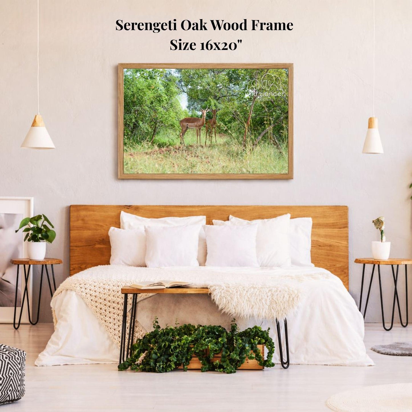a serene bedroom scene with a large, 16x20" framed photograph of a deer standing in a lush, green forest. The photograph is hung on a wall above a bed with white bedding and pillows. The room has a wooden headboard and a wooden nightstand on each side of the bed, with a potted plant and a small plant on the nightstands. The overall atmosphere of the room is calm and peaceful, with the natural elements of the forest providing a sense of tranquility.