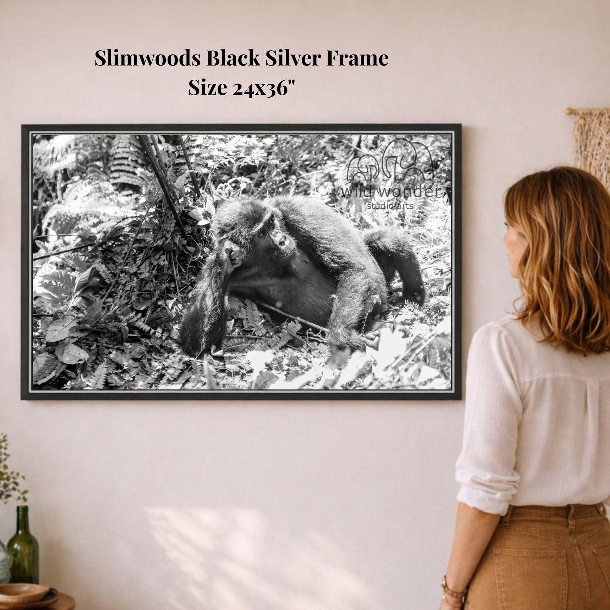 A woman is standing in front of a framed black and white photograph of a monkey in a forest setting.