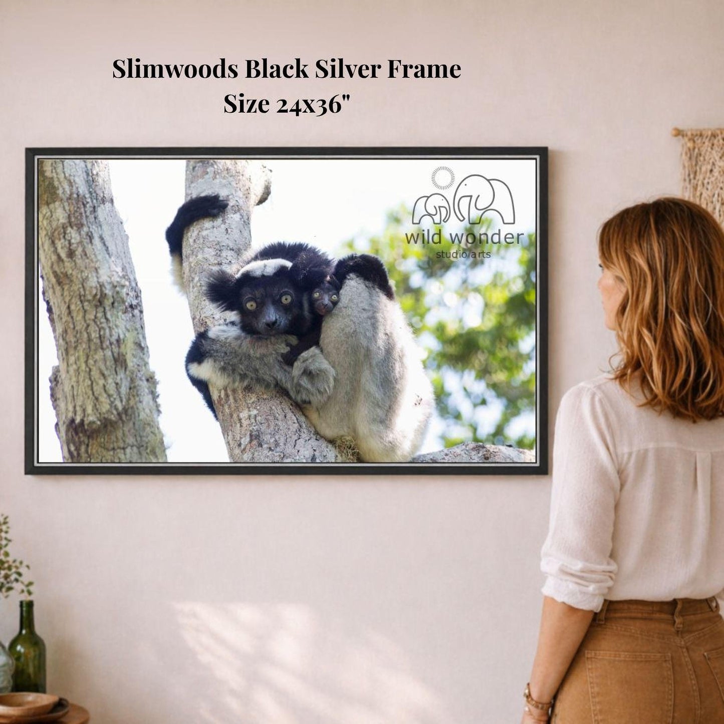 A woman is standing in front of a framed photograph of a lemur on a tree branch, looking at the picture.