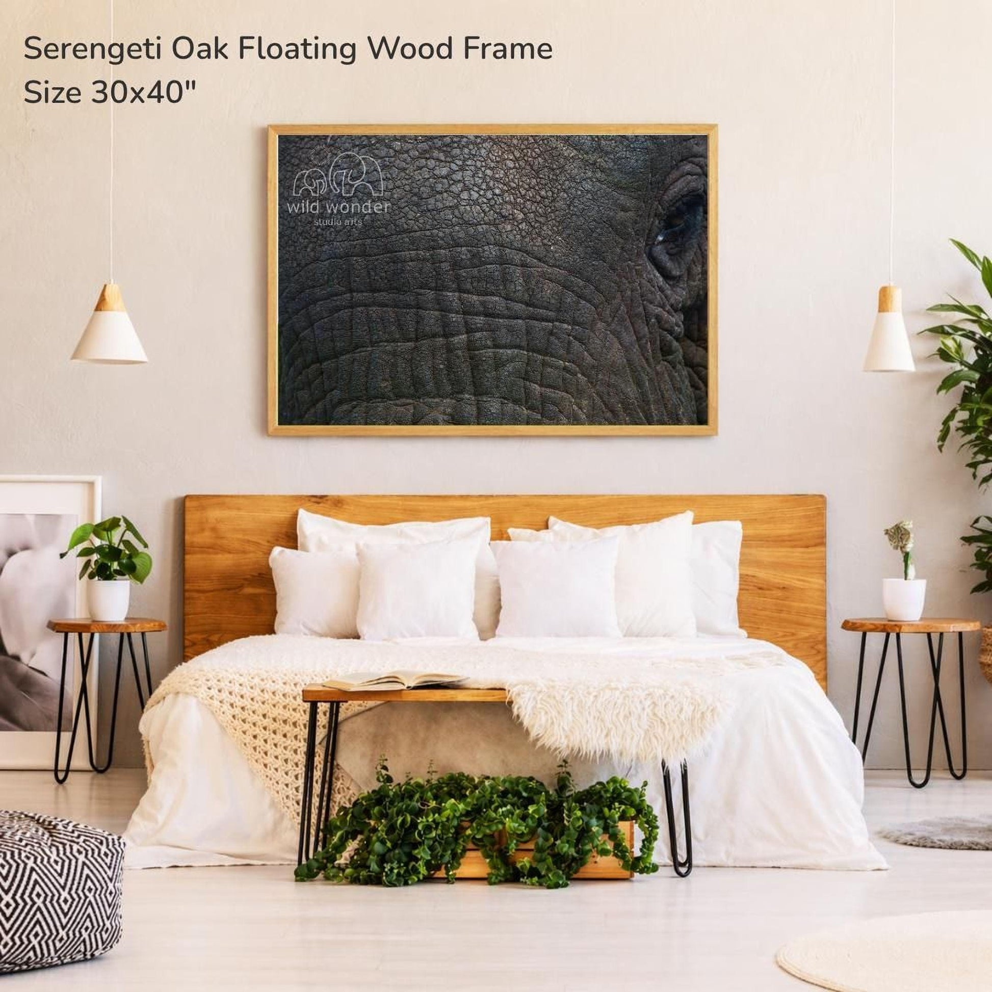 a serene bedroom setting with a large bed, a wooden headboard, and a framed photograph of an elephant's eye on the wall. The room has a minimalist and modern design, with pendant lights hanging above the bed and a plant on the floor.