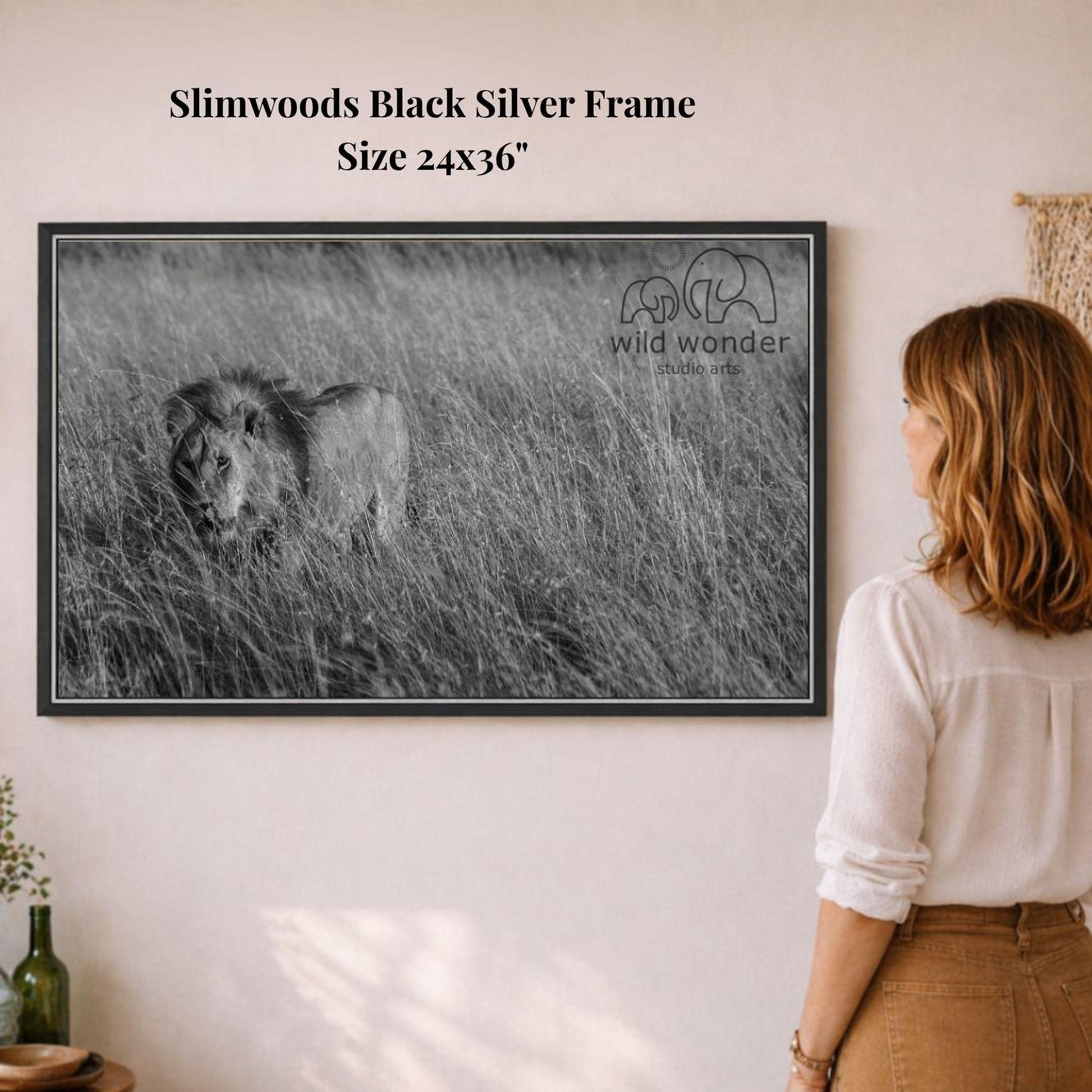 A woman is standing in front of a framed black and white photograph of a lion in a grassy field, looking at the artwork.