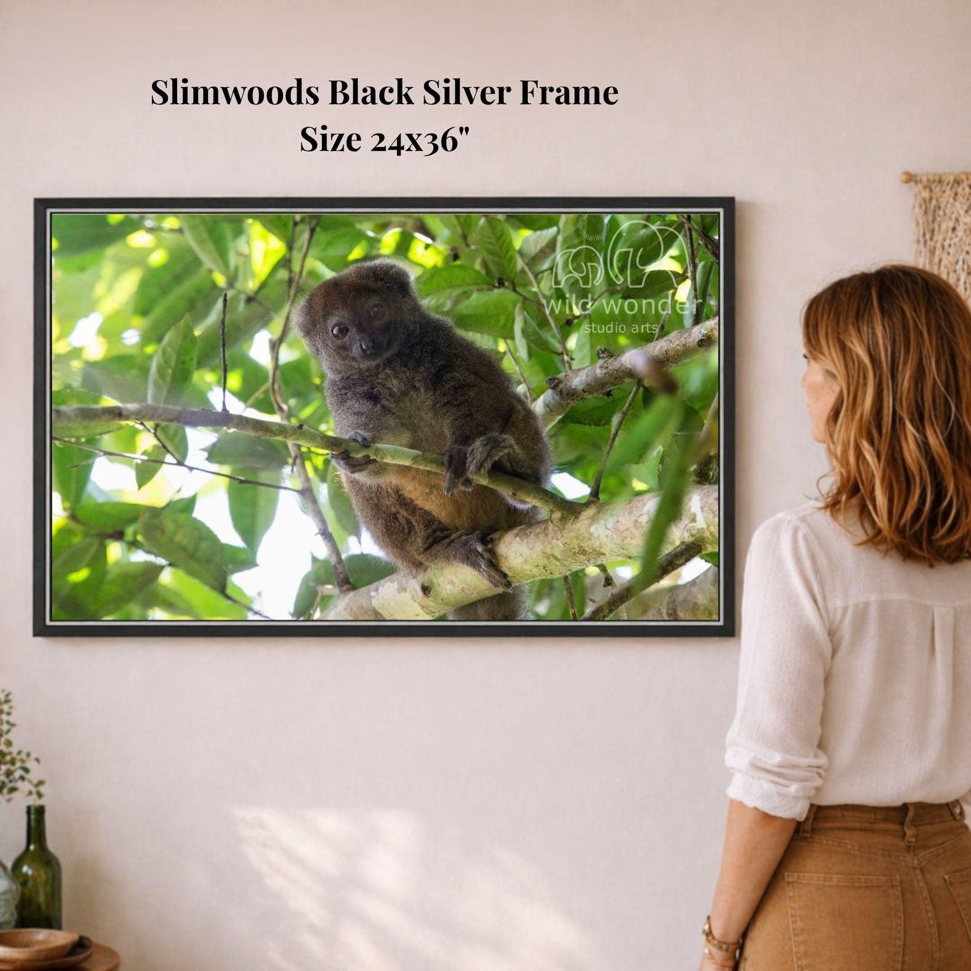 A woman is standing in front of a framed photograph of a koala bear perched on a tree branch, which is hanging on a wall.