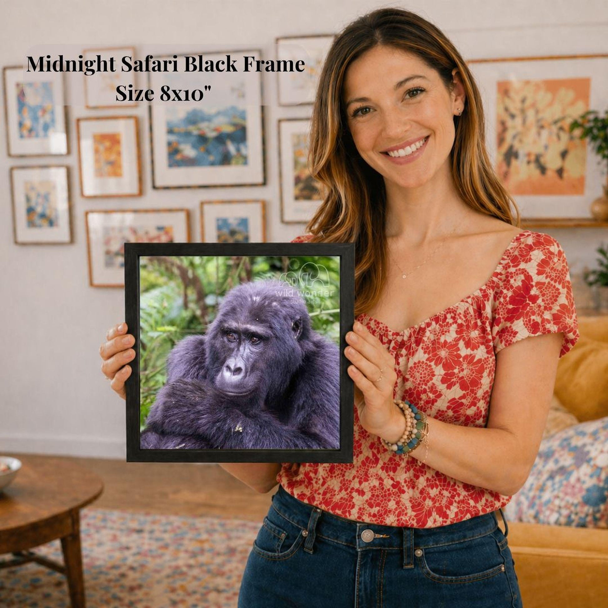 A woman is holding a framed picture of a gorilla in a room with various framed pictures on the walls.