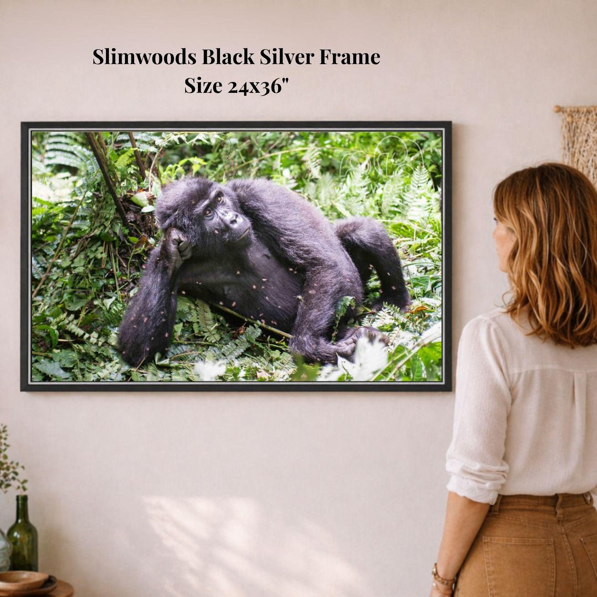 A woman is standing in front of a framed photograph of a gorilla in a lush, green forest environment.