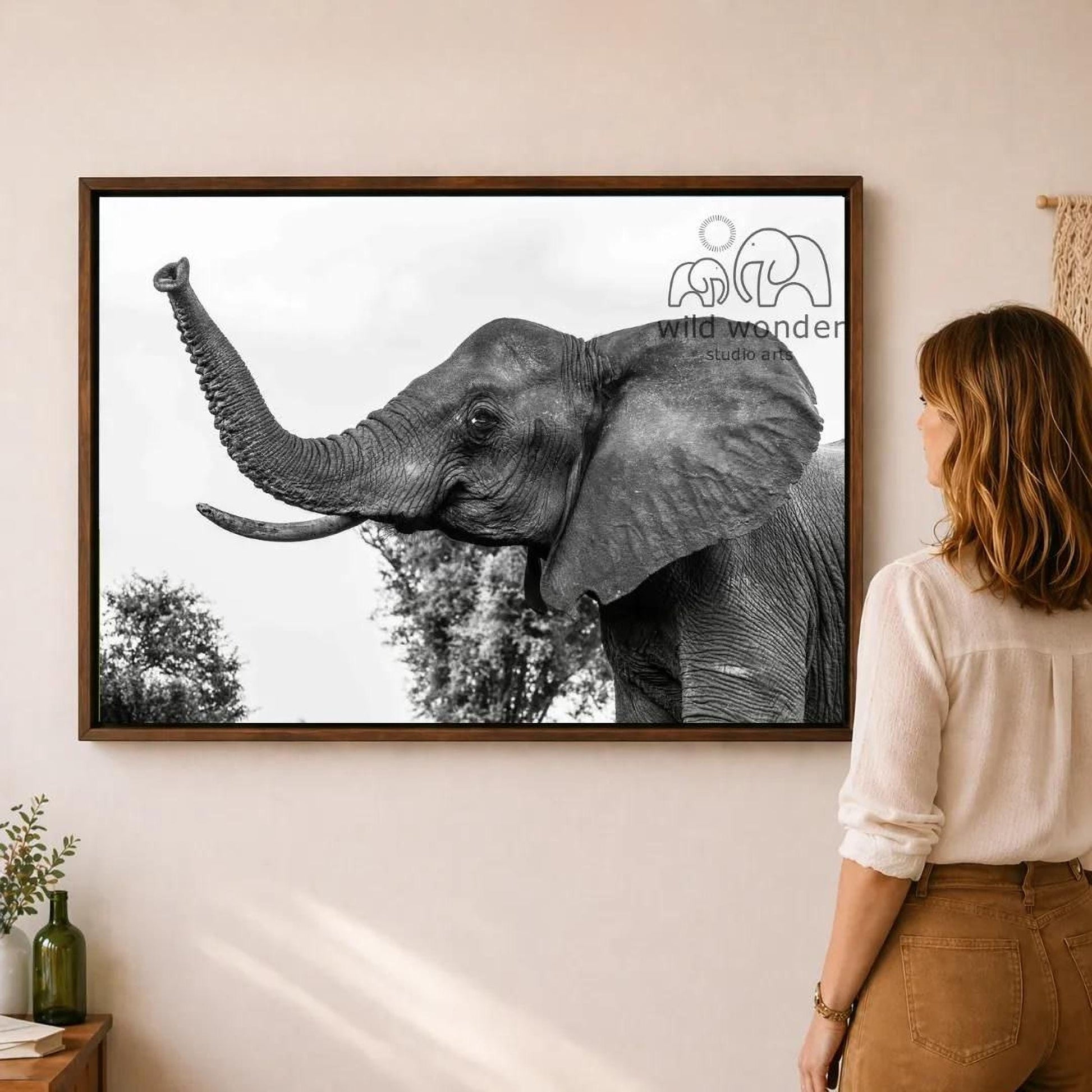 A woman is standing in front of a framed photograph of an elephant, looking at the artwork on the wall.