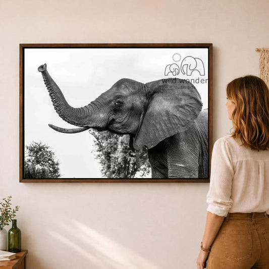 A woman is standing in front of a framed photograph of an elephant, looking at the artwork on the wall.