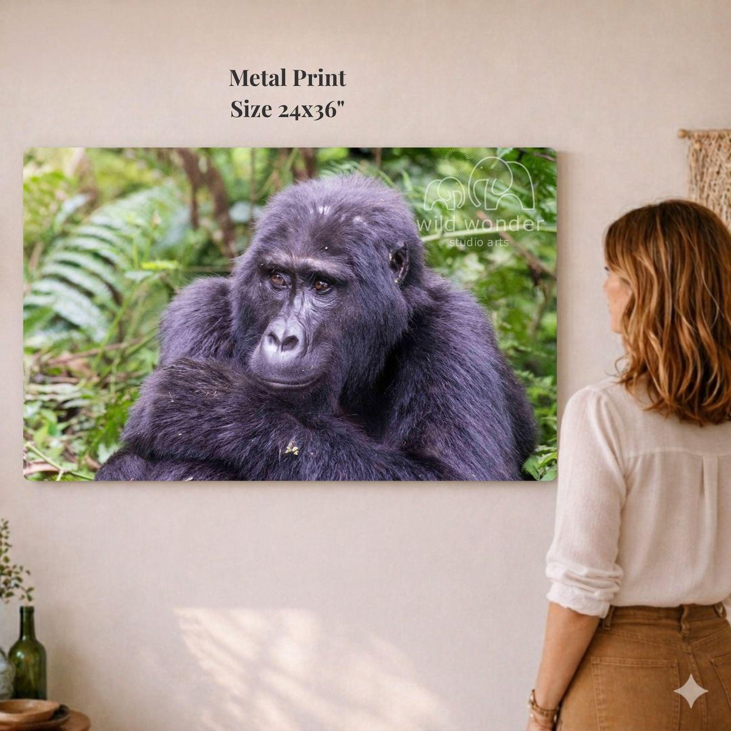 A woman is standing in front of a large metal print depicting a gorilla in a lush, green forest environment.