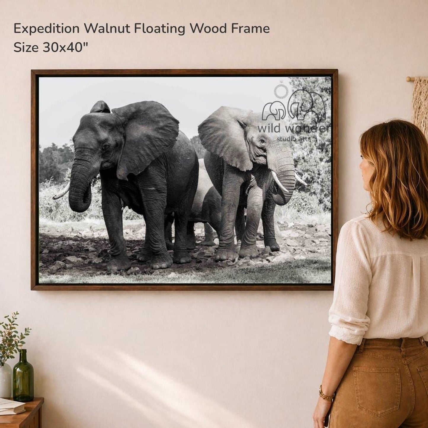 A woman is standing in front of a framed photograph of two elephants, one larger and one smaller, in a natural setting.