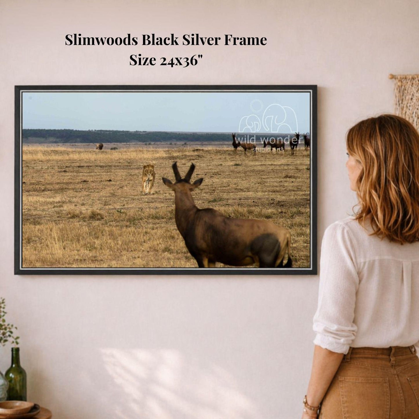 A woman is standing in front of a framed photograph of a wild animal, such as a lion or a wildebeest, in a grassy field.