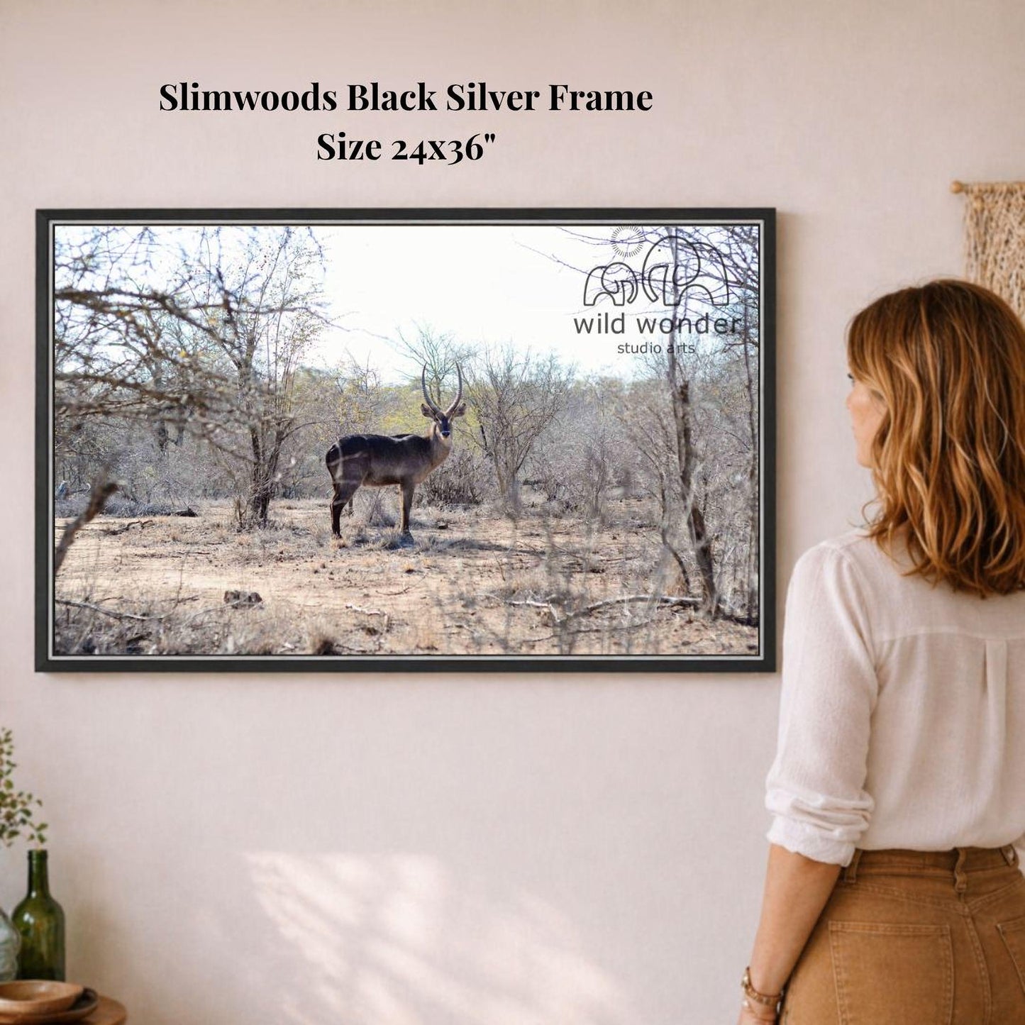 A woman is standing in front of a framed photograph of a deer in a forest setting, looking at the artwork.