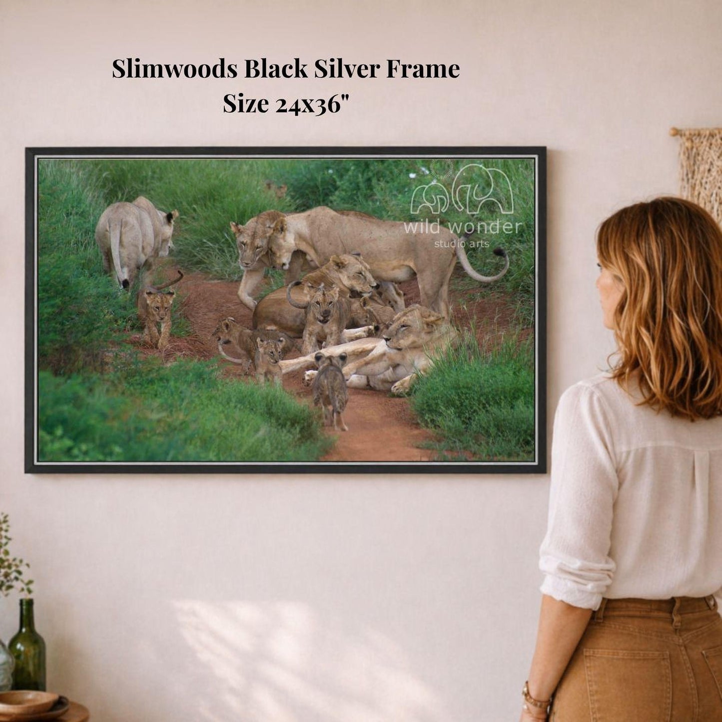 A woman is standing in front of a framed photograph of a group of lions in a natural setting.