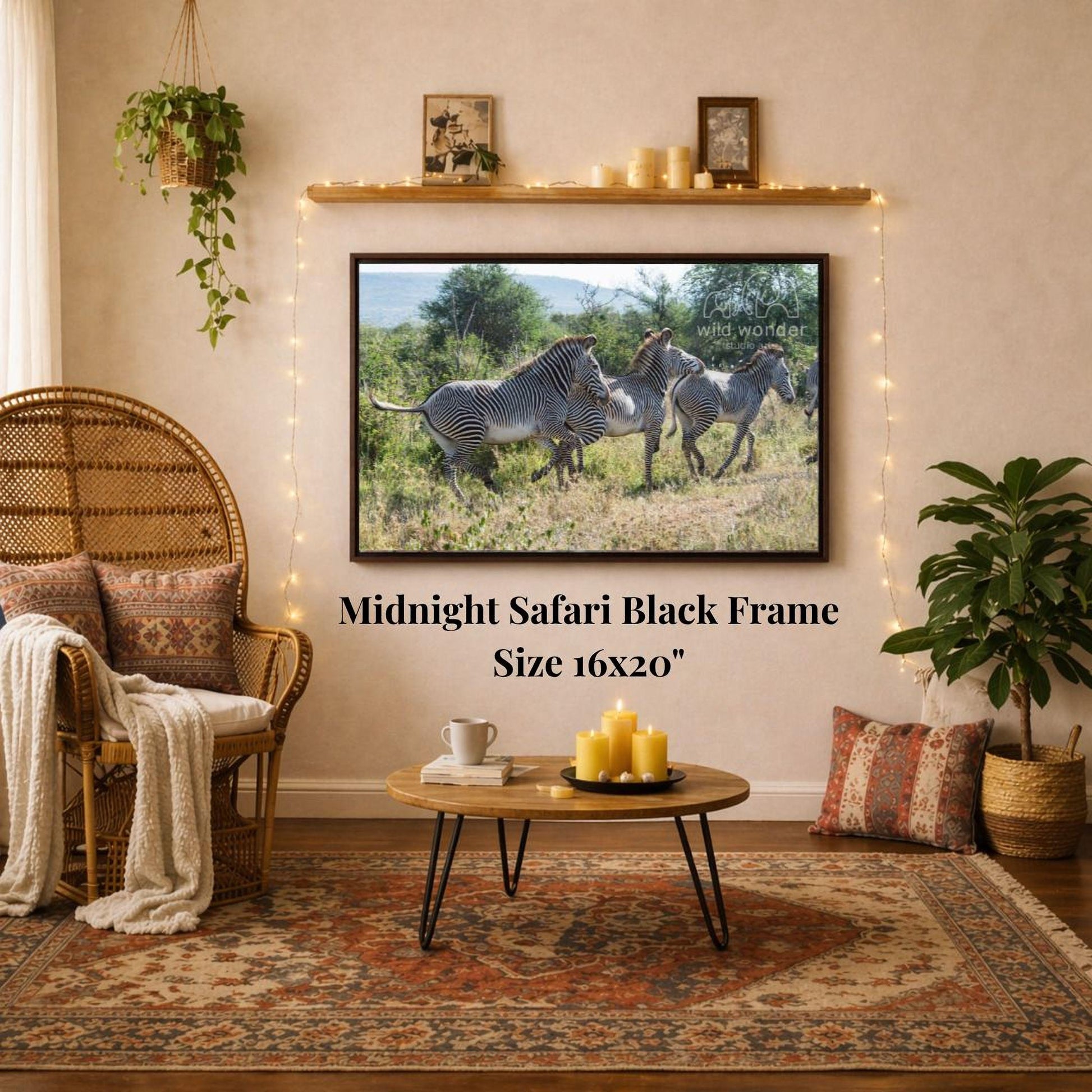 a living room with a large framed photograph of three zebras in a grassy field hanging on the wall. The photograph is framed in a black frame and is the focal point of the room. The room is decorated with a wicker chair, a coffee table, and a potted plant, creating a cozy and inviting atmosphere.