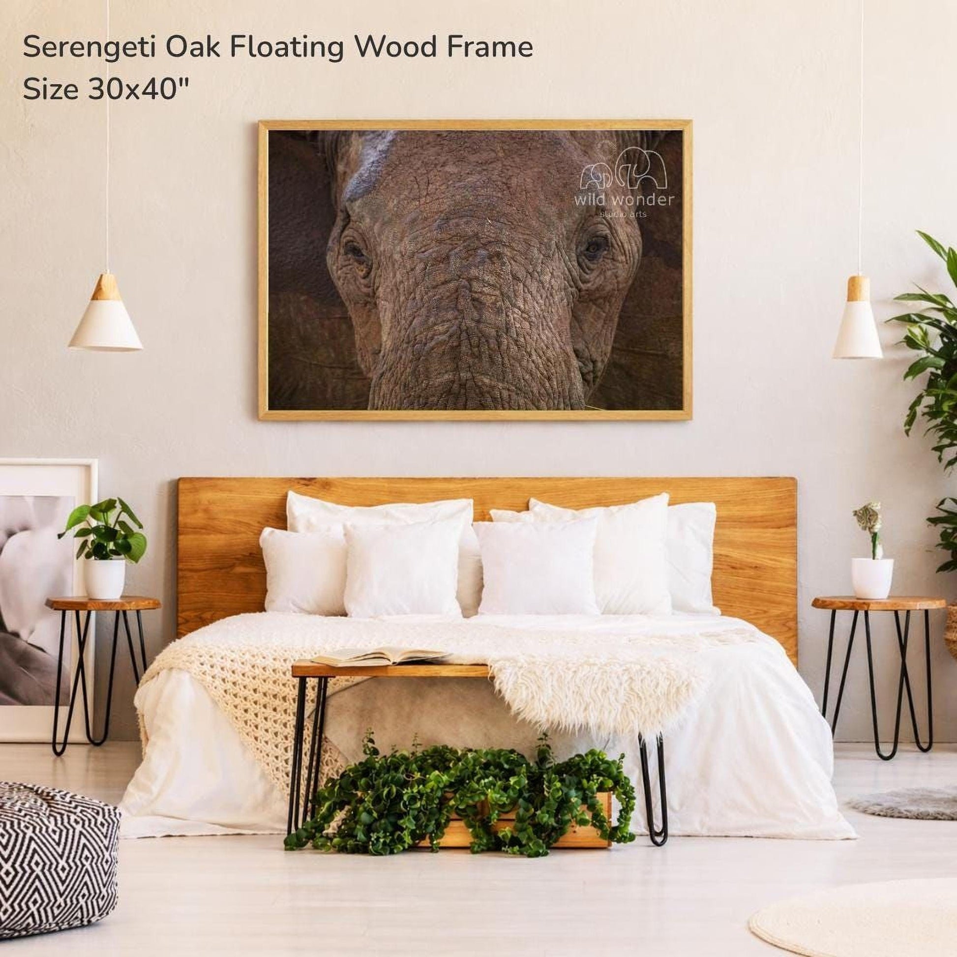 a bedroom with a large wooden headboard and a white bedspread. Above the bed is a framed photograph of an elephant's face, which appears to be a serene and calming image. The room also includes a potted plant, a vase, and a rug, creating a cozy and inviting atmosphere.