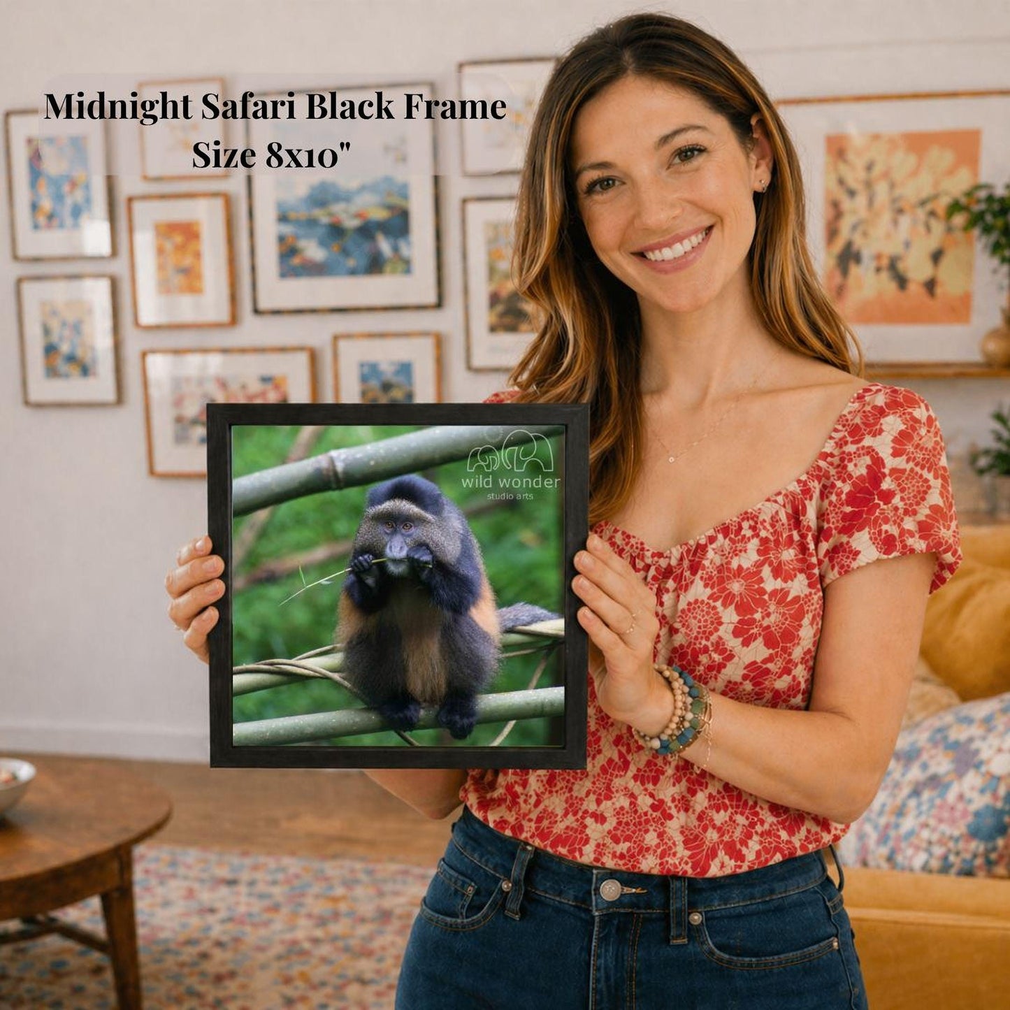 A woman is holding a framed photograph of a monkey in a forest setting, with a smiling expression on her face.