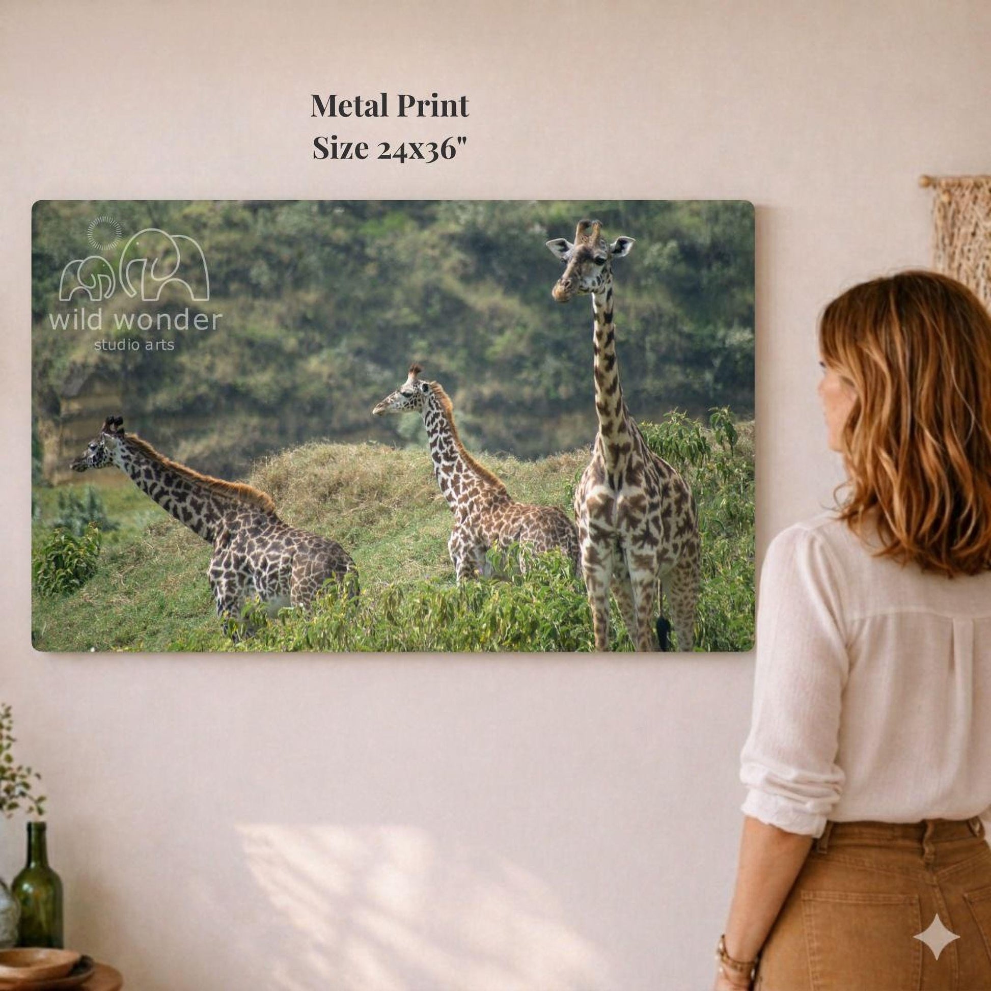 A woman is standing in front of a large metal print depicting three giraffes in a grassy field.