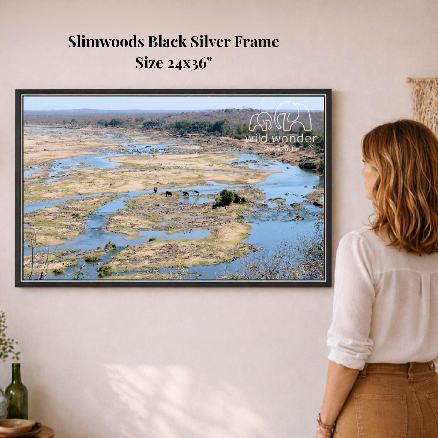 A woman is standing in front of a framed photograph of a scenic landscape, which appears to be a river or stream surrounded by vegetation.