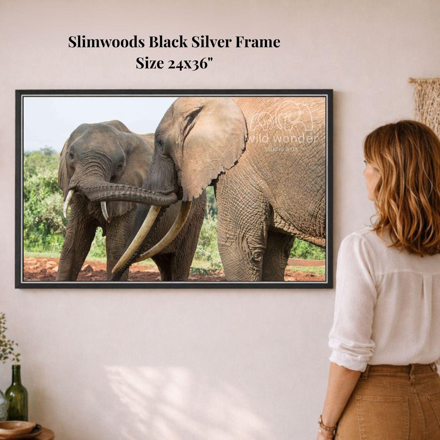 A woman is standing in front of a framed photograph of two elephants, one larger and one smaller, in a natural setting.