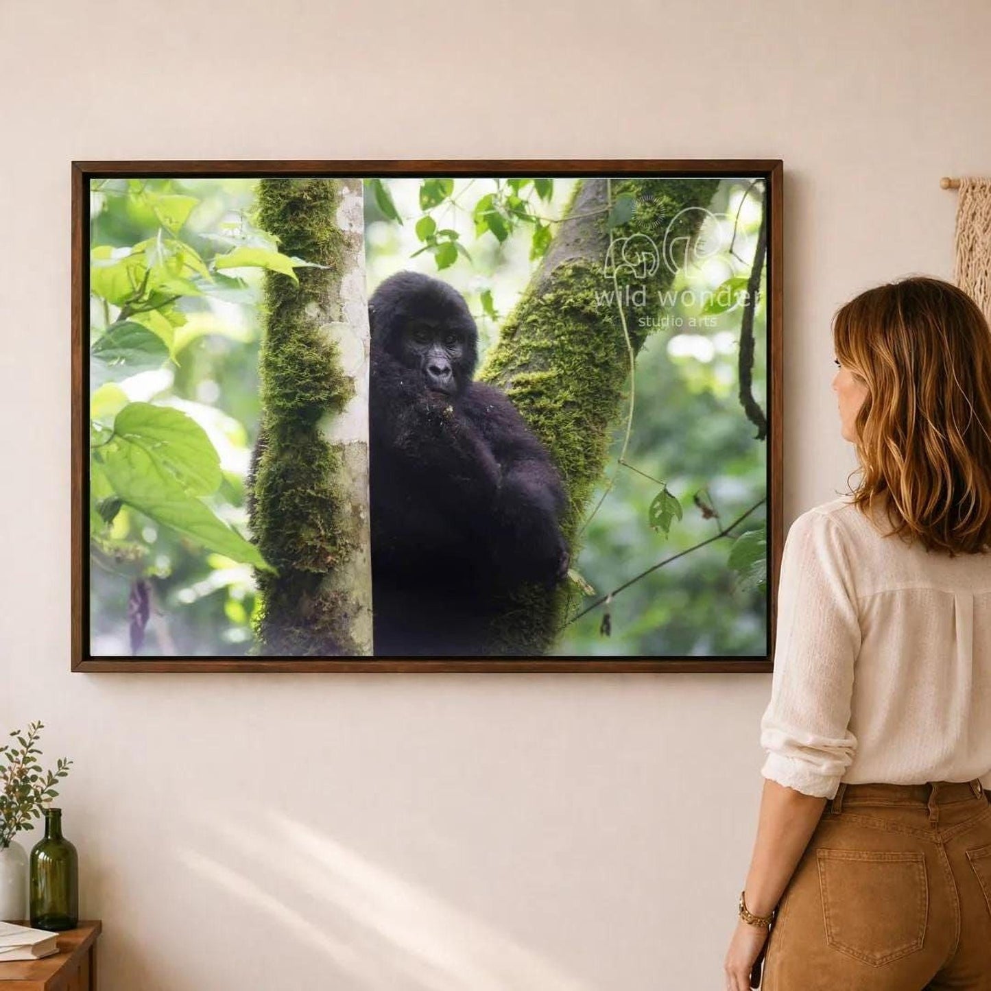 A woman is standing in front of a framed photograph of a gorilla on a tree, looking at the artwork.