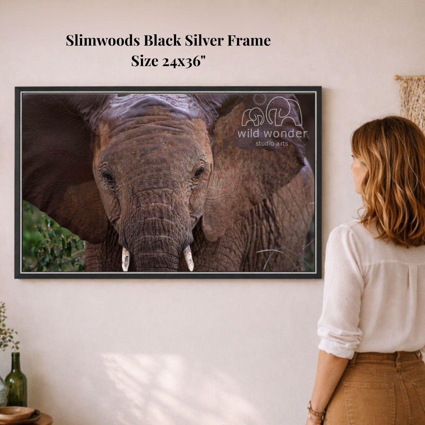 A woman is standing in front of a framed photograph of an elephant, looking at it with interest.