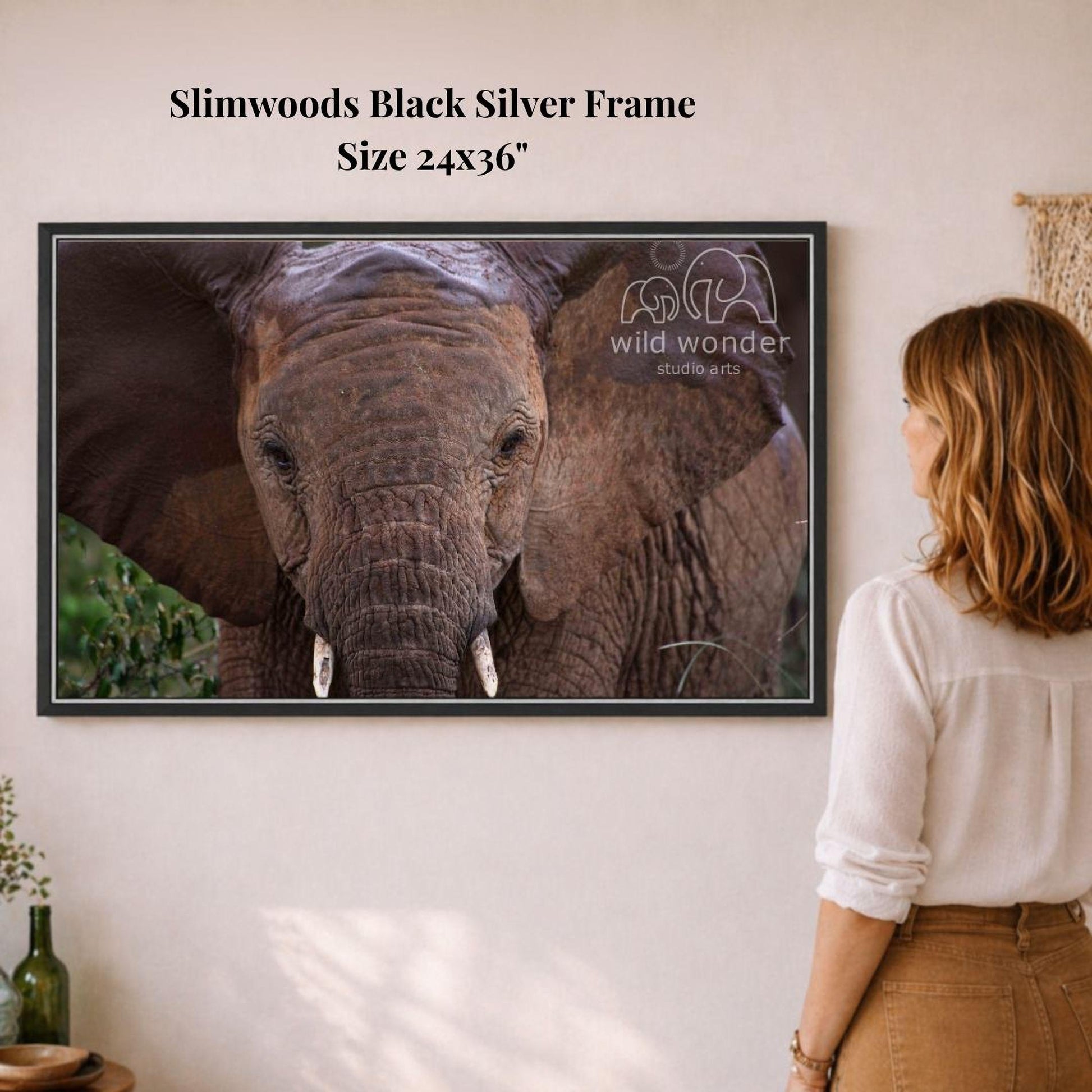 A woman is standing in front of a framed photograph of an elephant, looking at it with interest.
