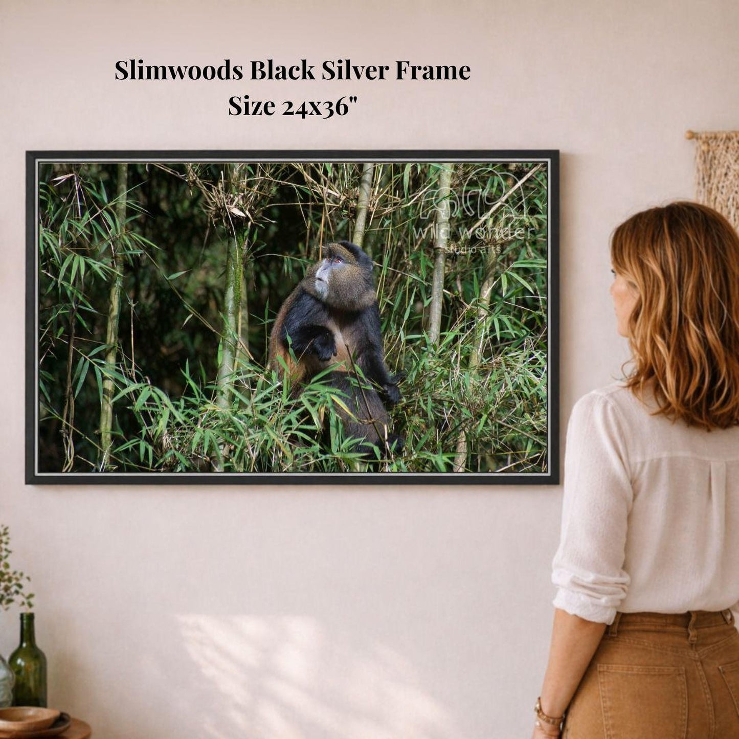 A woman is standing in front of a framed photograph of a monkey in a lush, green forest environment.