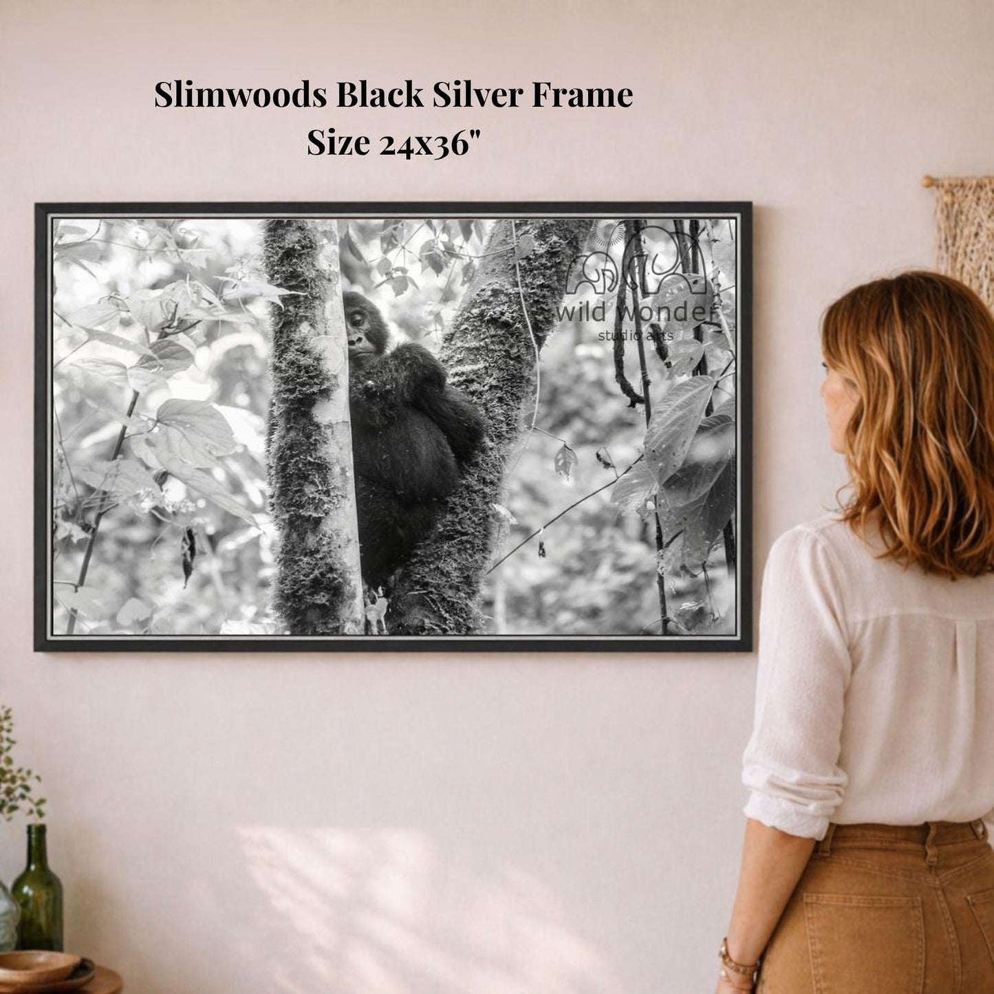 A woman is standing in front of a framed black and white photograph of a gorilla climbing a tree.
