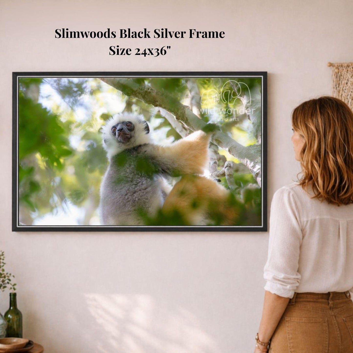 A woman is standing in front of a framed photograph of a lemur in a tree, looking at the artwork on the wall.