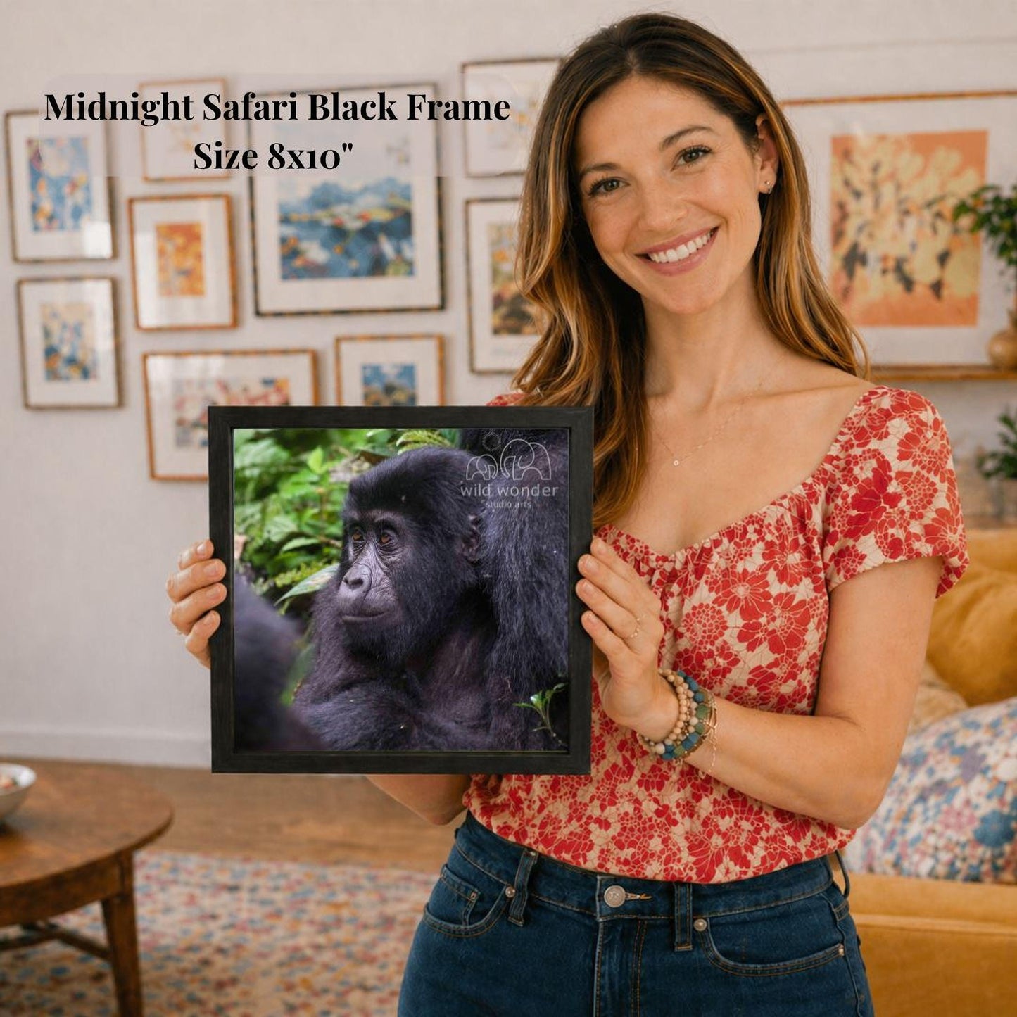 A woman is holding a framed photograph of a gorilla in a natural setting, with a smiling expression on her face.