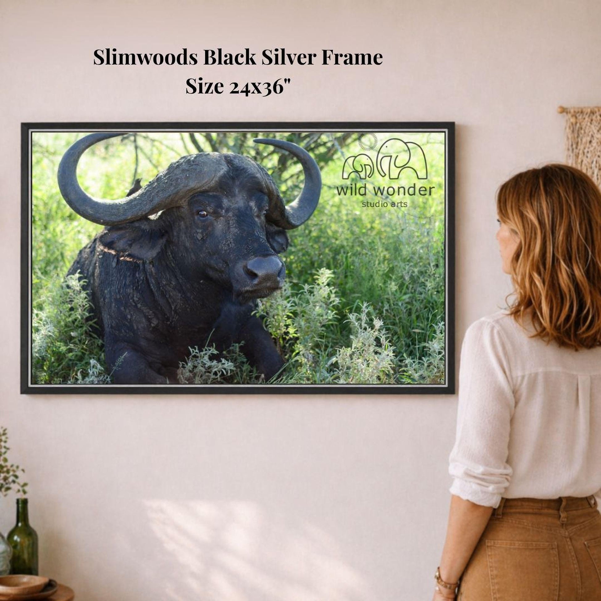 A woman is standing in front of a framed photograph of a black buffalo with large horns, which is hanging on a wall.