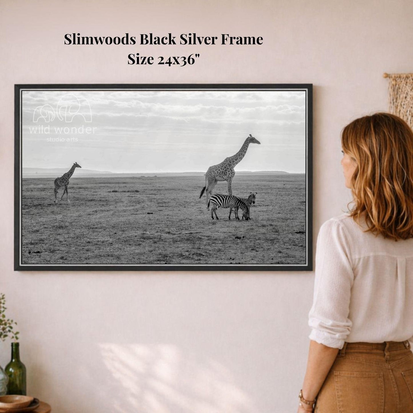 A woman is standing in front of a framed black and white photograph of three giraffes and a zebra in a savanna-like setting.