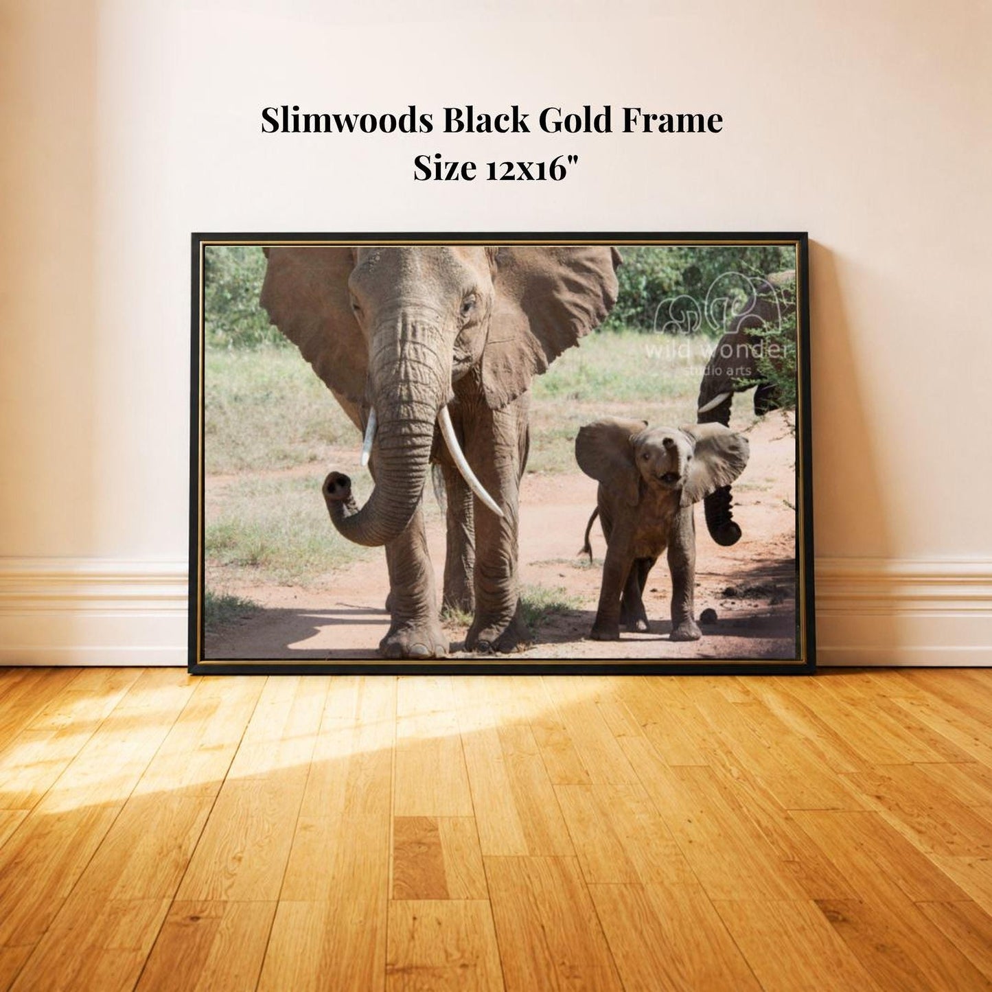 A black gold frame containing a photograph of two elephants, one adult and one juvenile, standing on a dirt path surrounded by trees.