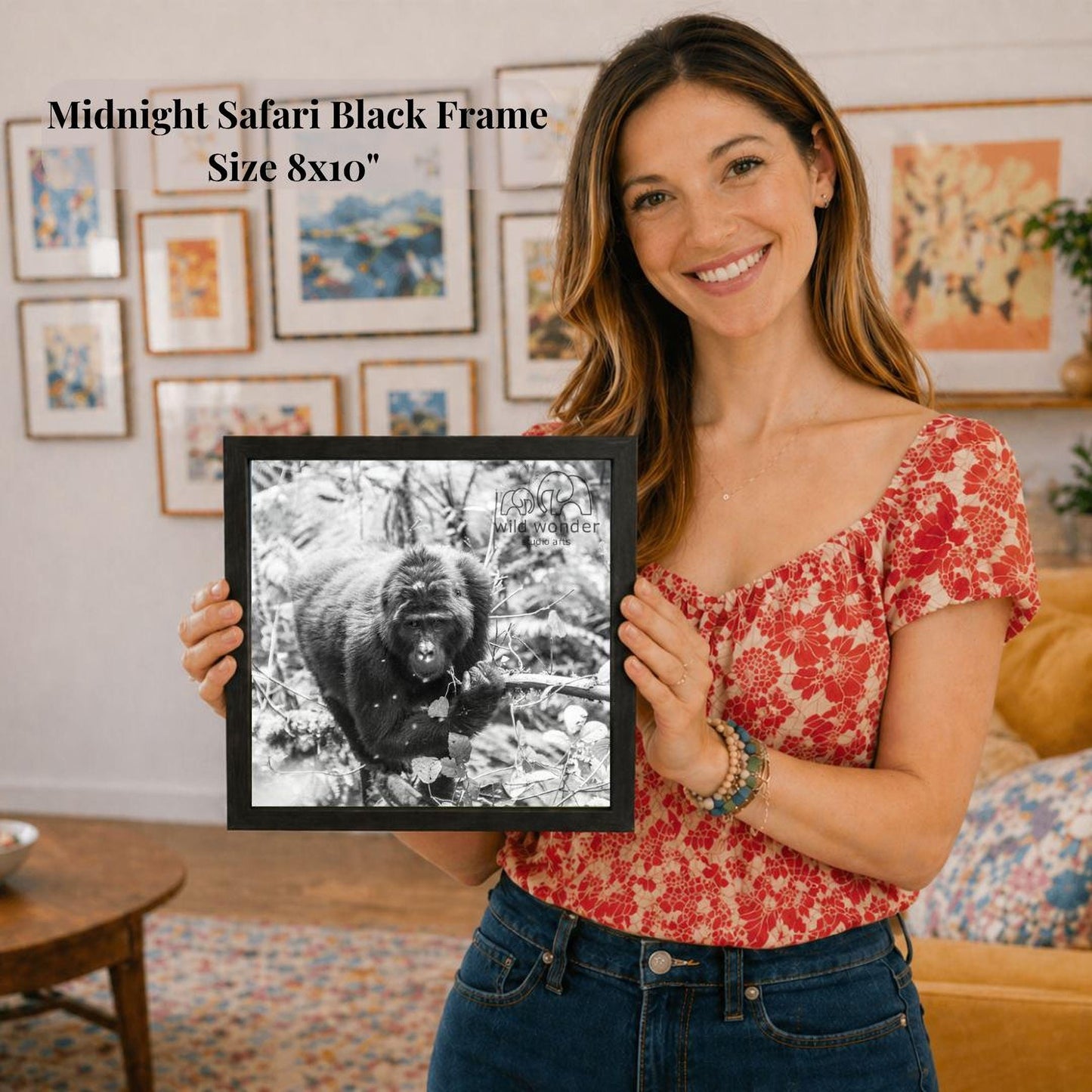 A woman is holding a framed black and white photograph of a gorilla in a forest, with a smiling expression on her face.