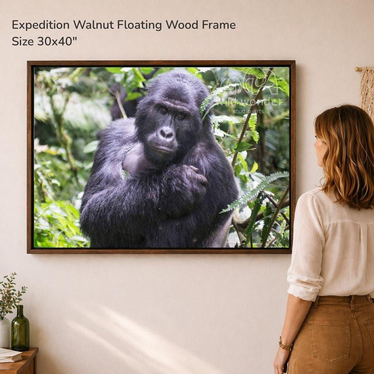 A woman is standing in front of a large framed photograph of a gorilla in a forest setting, looking at the artwork.