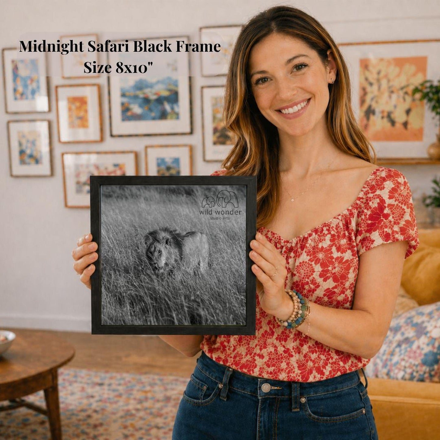 A woman is holding a framed photograph of a lion in a grassy field, smiling and posing for the camera.