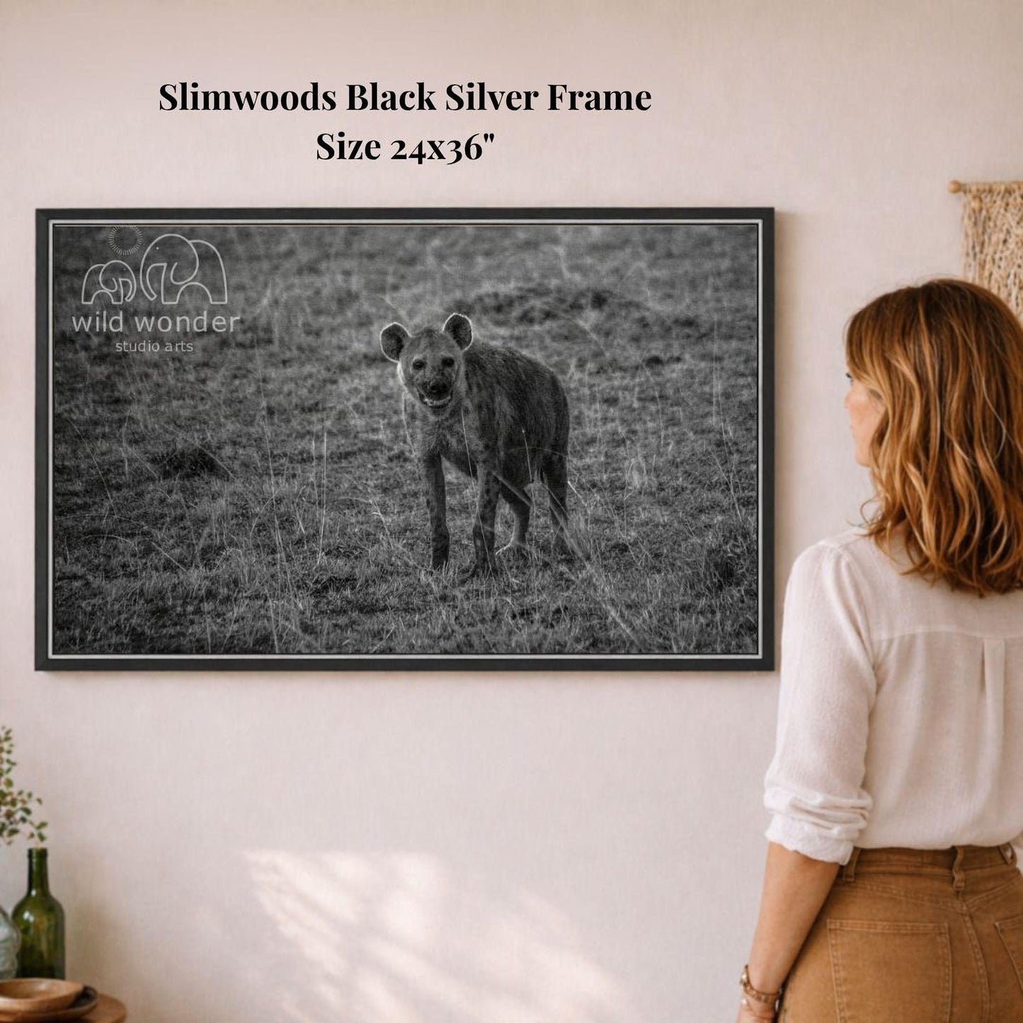 A woman is standing in front of a framed black and white photograph of a hyena in a grassy field.