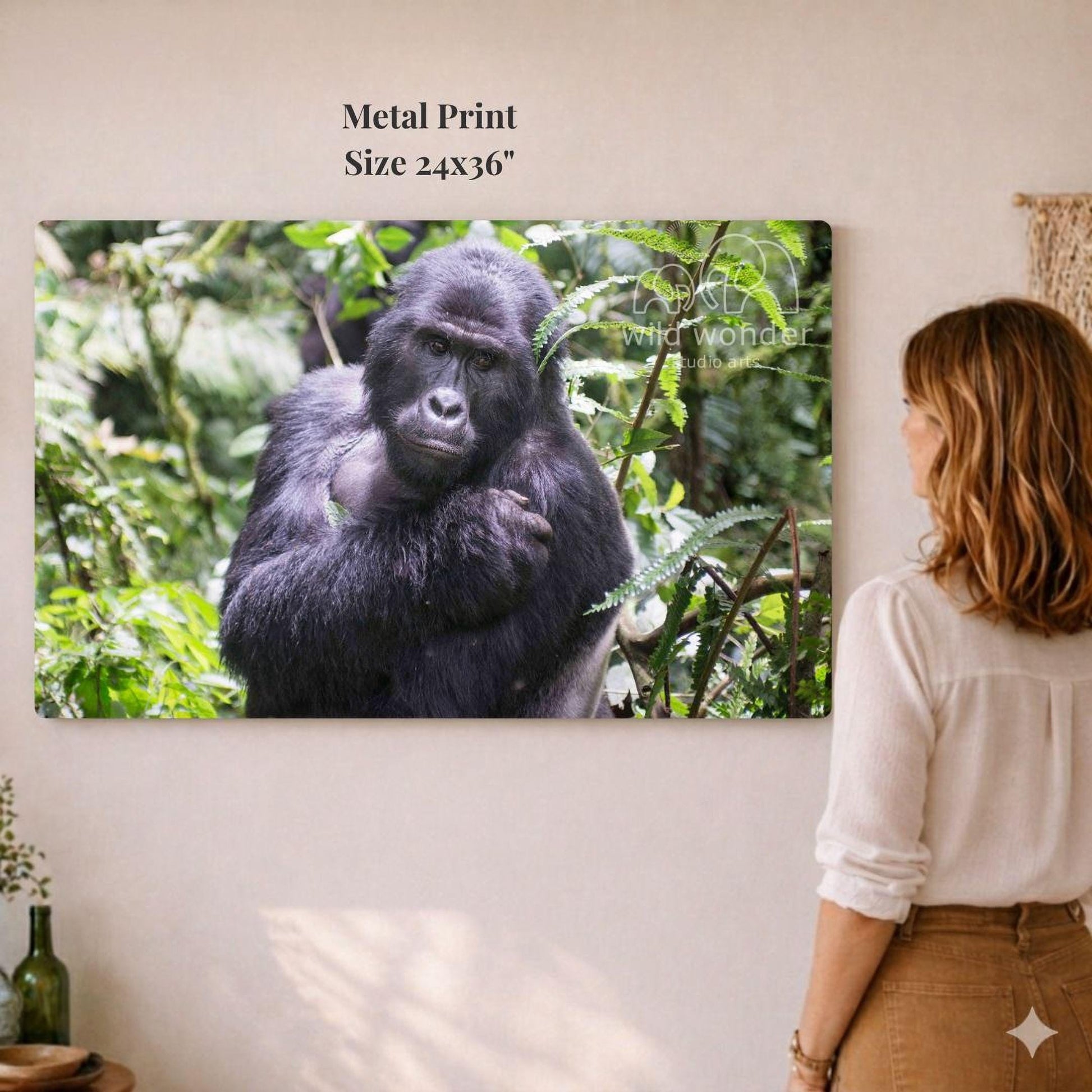 A woman is standing in front of a large metal print depicting a gorilla in a lush, green forest environment.