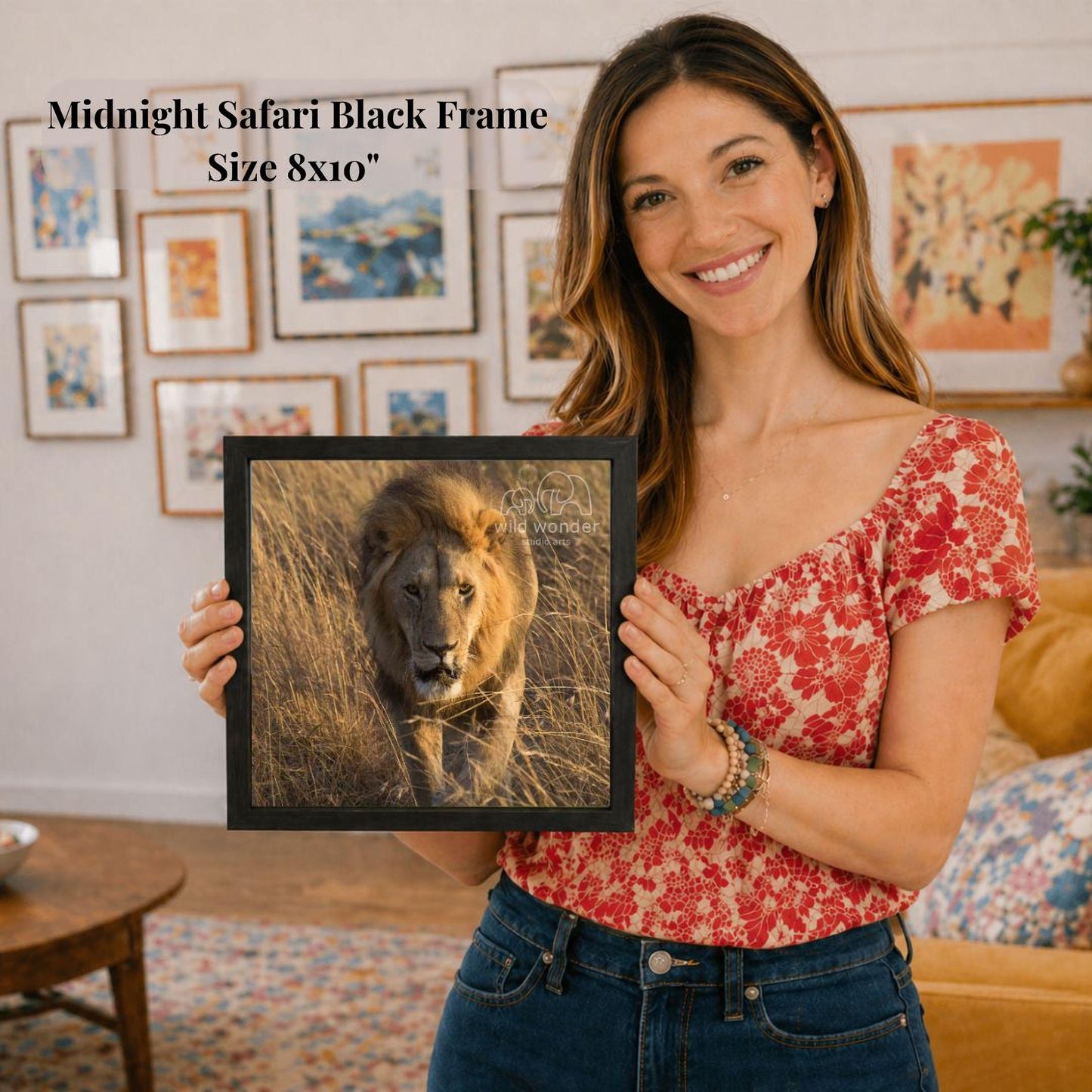 A woman is holding a framed photograph of a lion in a grassy field, smiling and posing for the camera.