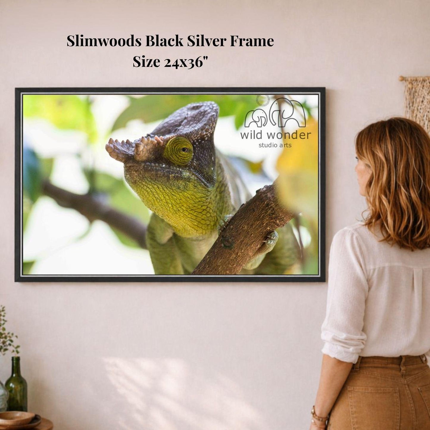 A woman is standing in front of a framed photograph of a chameleon on a branch, looking at the artwork.