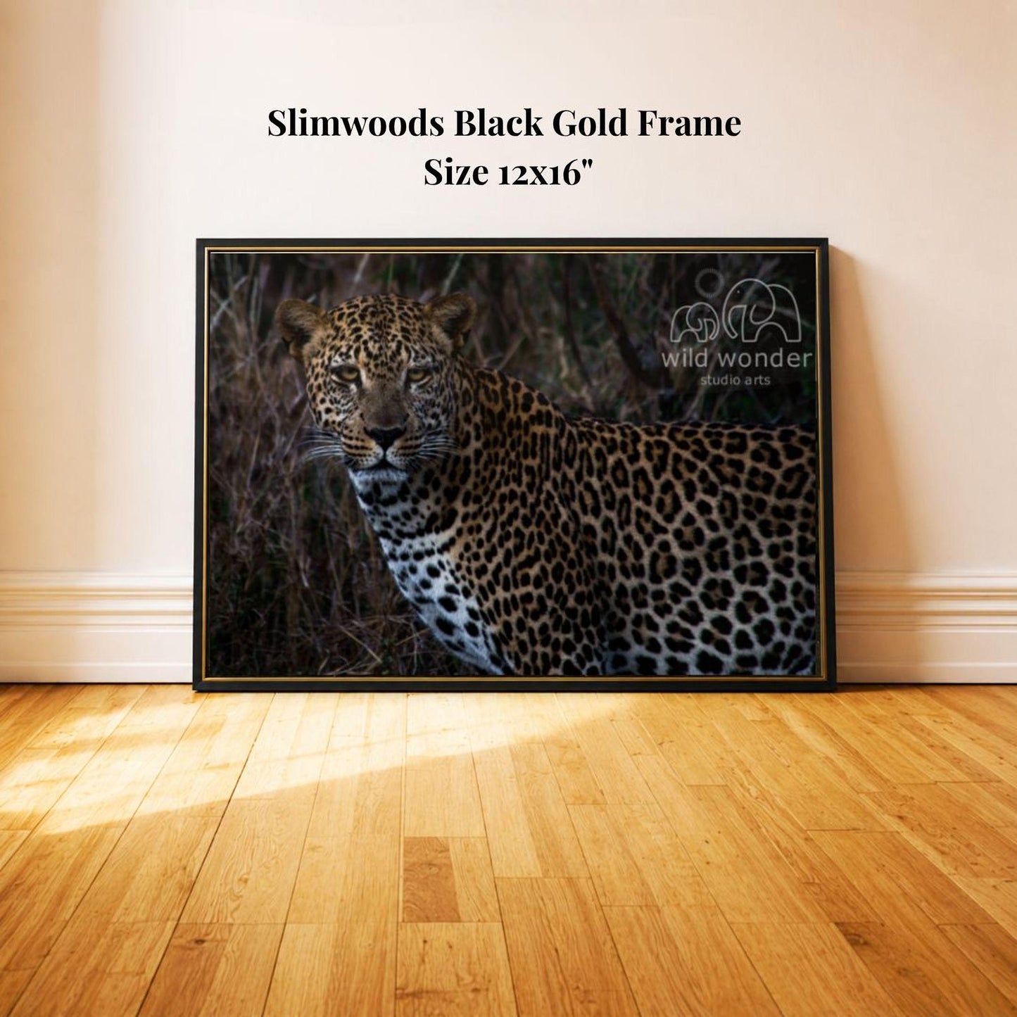 A framed photograph of a leopard is displayed on a wooden floor against a white wall.